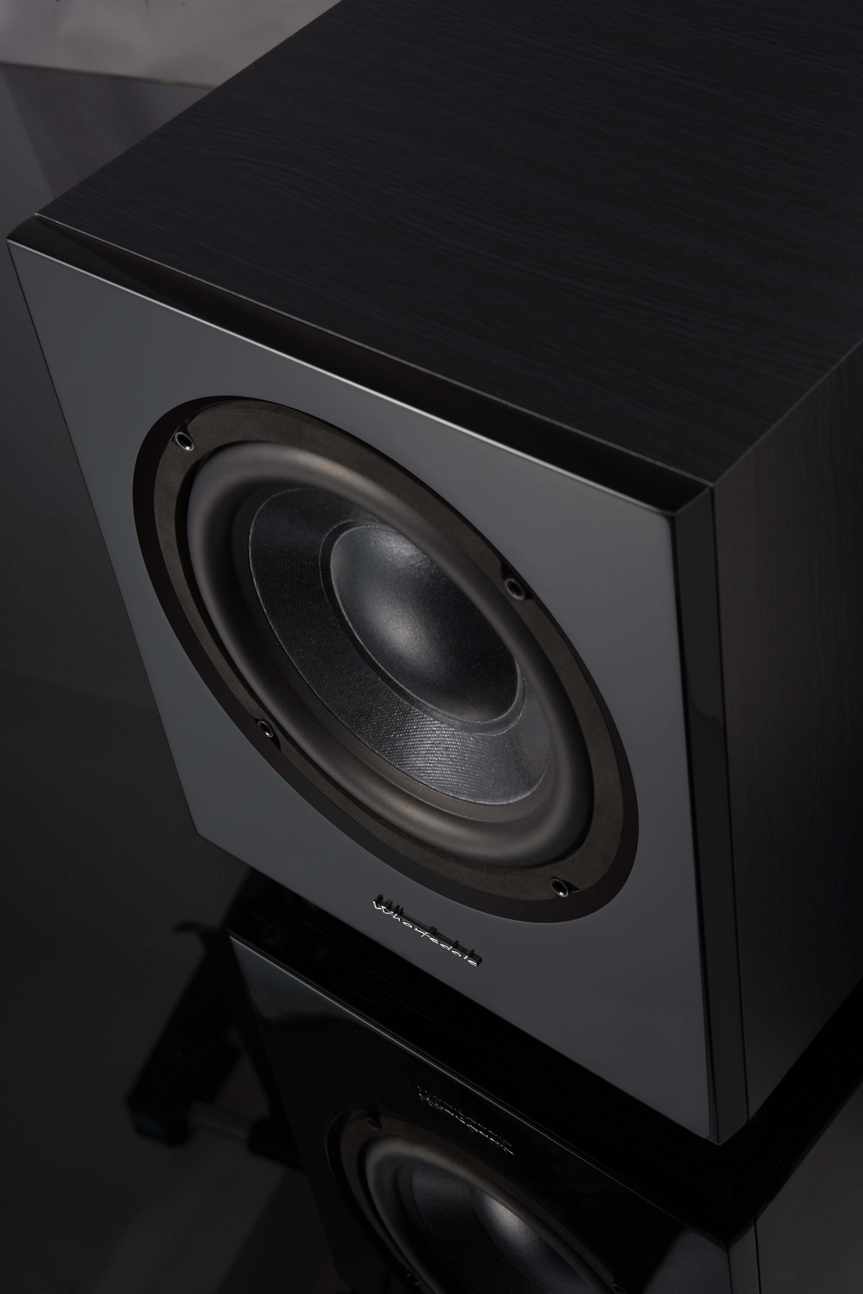 Caisson de basses Wharfedale noir. L'enceinte a une finition brillante et un grand haut-parleur circulaire.