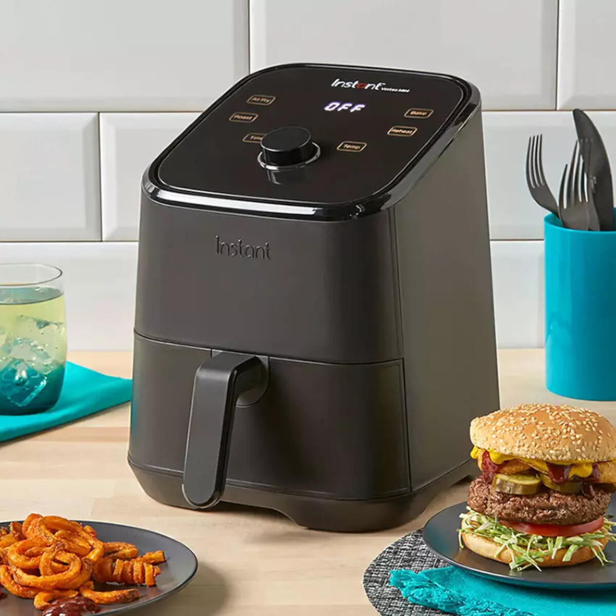Zwarte airfryer met eten, burger en drankje op een aanrecht.