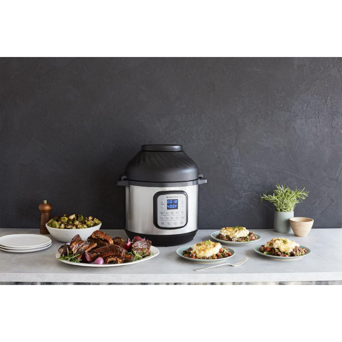 An Instant Pot with food on plates, surrounded by ingredients, on a dark countertop.