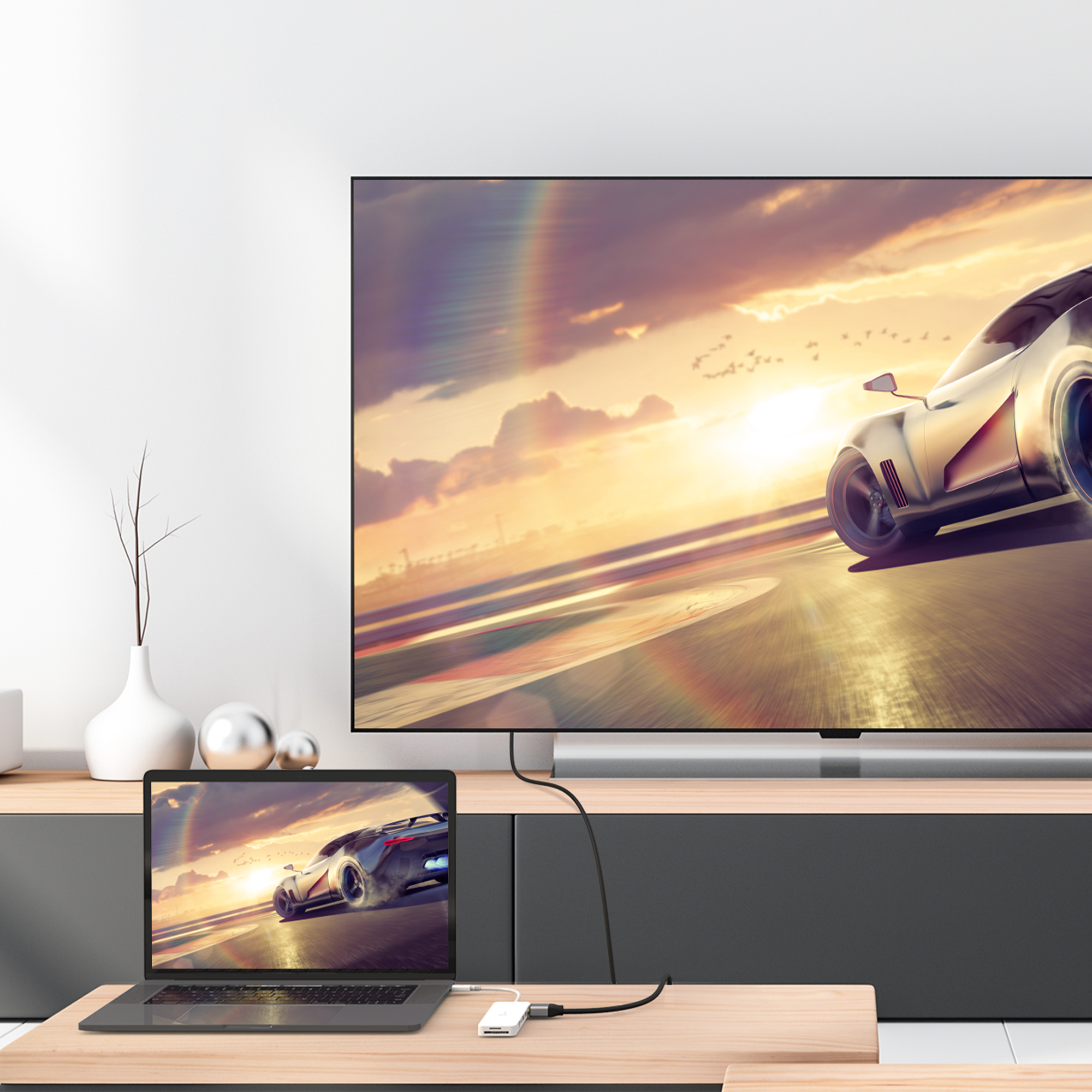 Laptop mit TV verbunden, zeigt eine Autorennszene. Vase und silberne Kugeln auf dem Tisch.