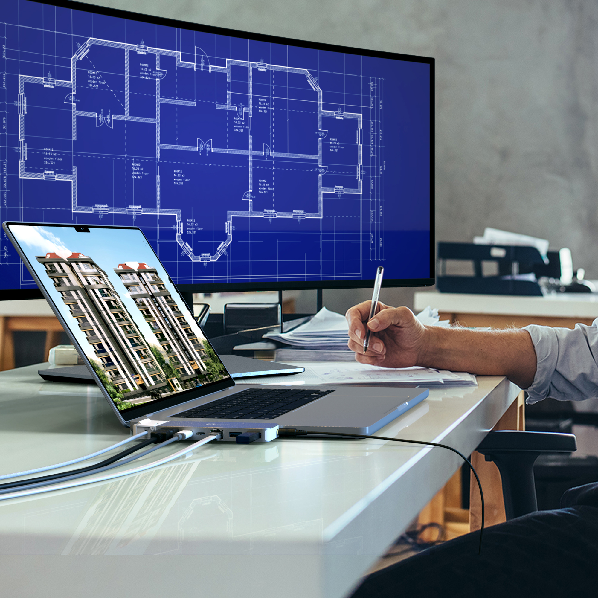 Eine Person arbeitet an einem Laptop und einem großen Monitor, beide zeigen Architekturpläne an.