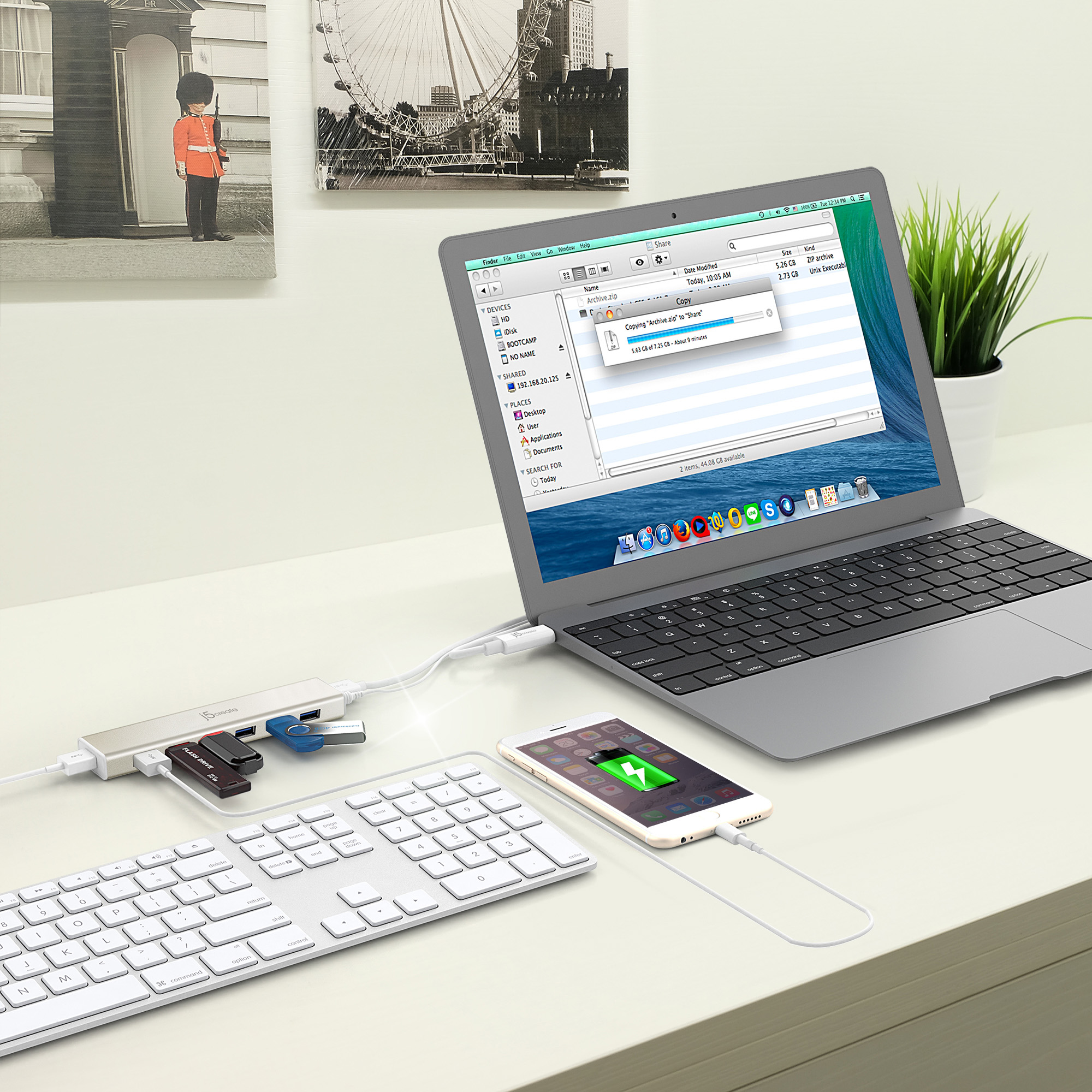 Laptop, USB-Hub, Tastatur und Telefon, das auf einem weißen Schreibtisch mit London-Bildhintergrund geladen wird.