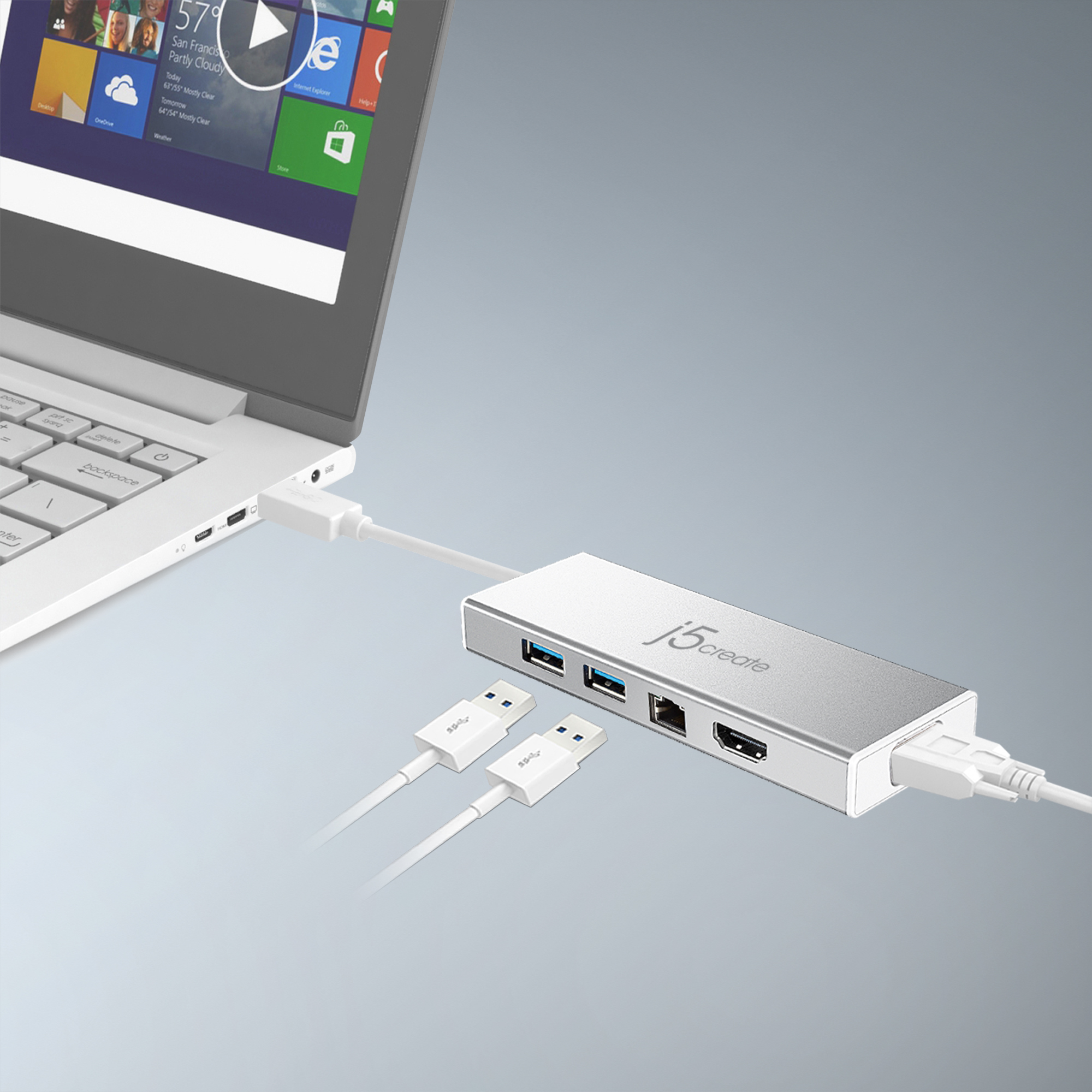 Ein silberner USB-Hub, der mit einem Laptop verbunden ist. Mehrere Anschlüsse sind sichtbar. Grauer Hintergrund.