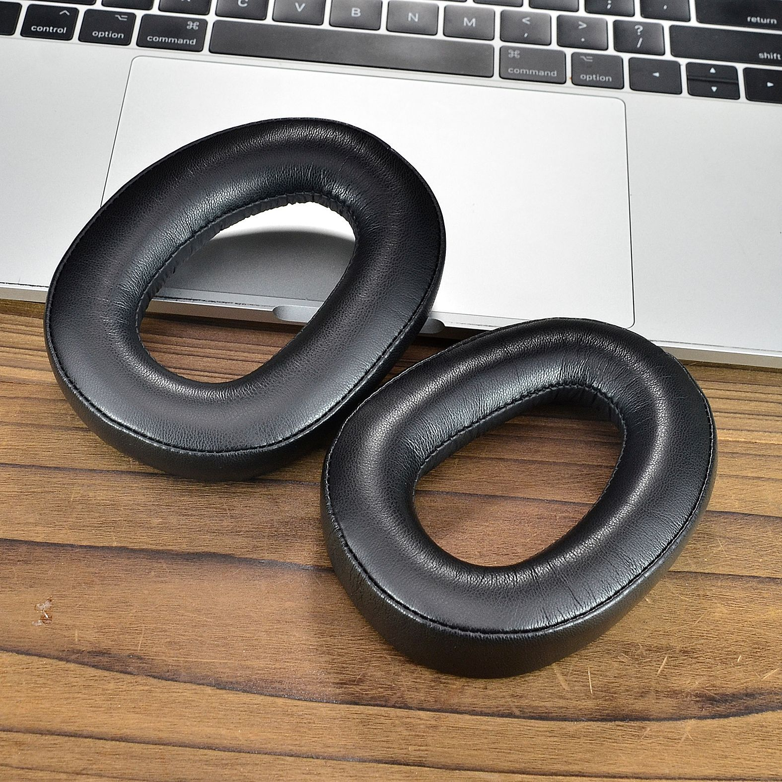 Twee zwarte oorkussens liggen op een houten tafel naast een laptoptoetsenbord.