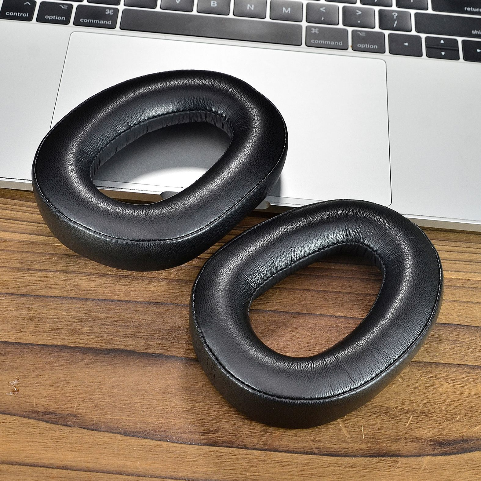 Twee zwarte oorkussens op een zilverkleurig laptoptoetsenbord. De kussens zijn ovaal en van leer.