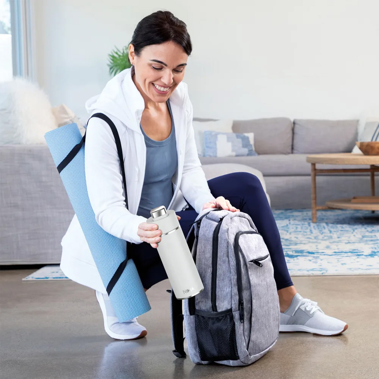 Donna che prepara una borsa da palestra. Tappetino yoga, borraccia e zaino visibili.