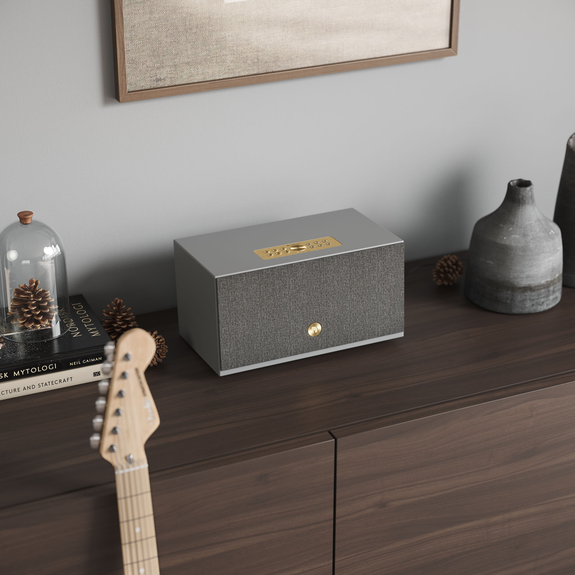 Altoparlante grigio moderno su un mobile in legno, libri e chitarra in primo piano. Articoli decorativi.
