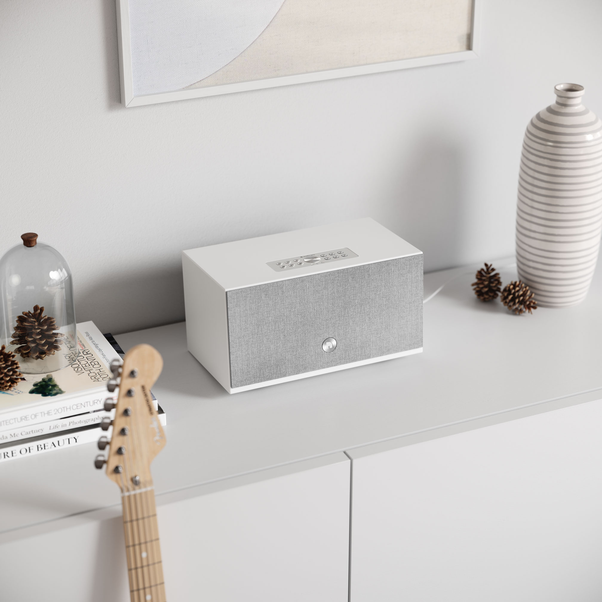 Altoparlante bianco su un mobile bianco con libri, chitarra e oggetti decorativi. Schema colori neutro.