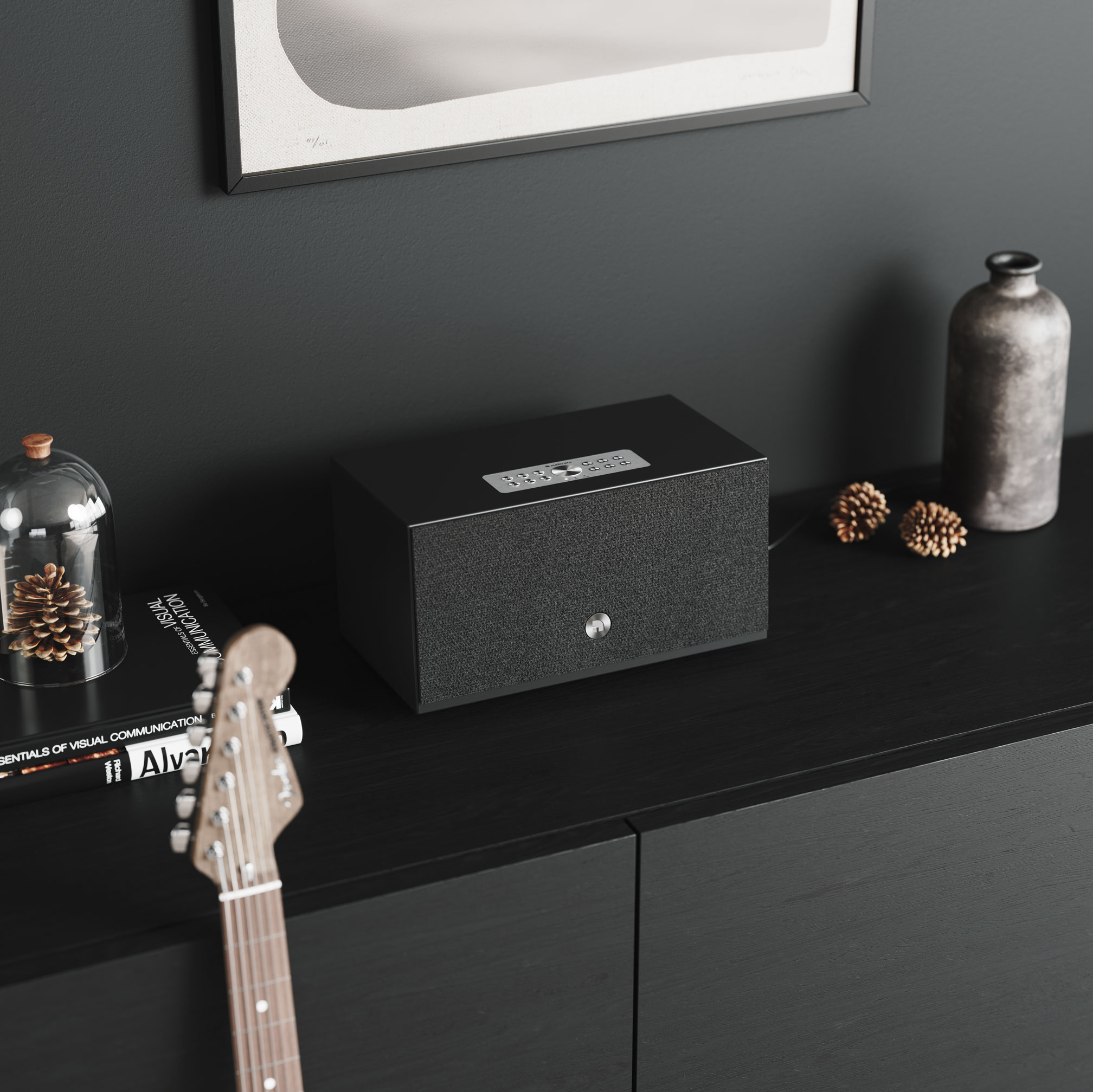 Altoparlante nero su un mobile in legno scuro con chitarra e decorazioni. Luce soffusa.