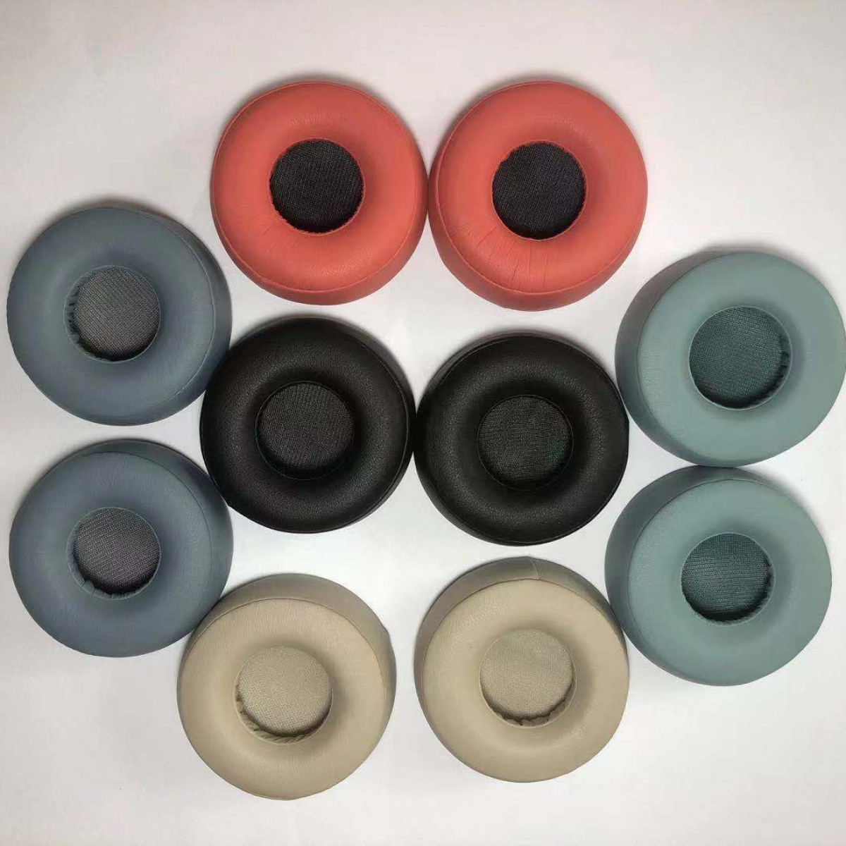 Neun kreisförmige Ohrpolster in verschiedenen Farben: blau, grau, rot, schwarz und beige, in einem Kreis angeordnet.