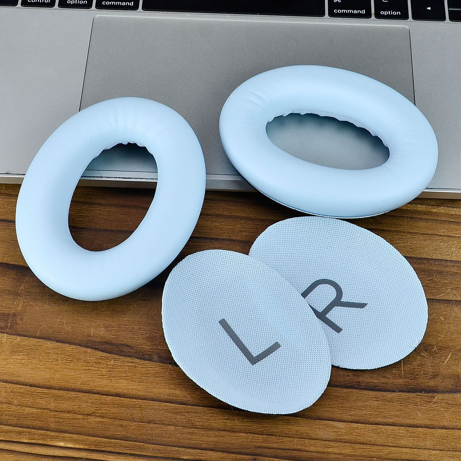 Nauszniki i wkładki do słuchawek na drewnianej powierzchni. Poduszki są jasnoniebieskie, wkładki z oznaczeniami L i R.