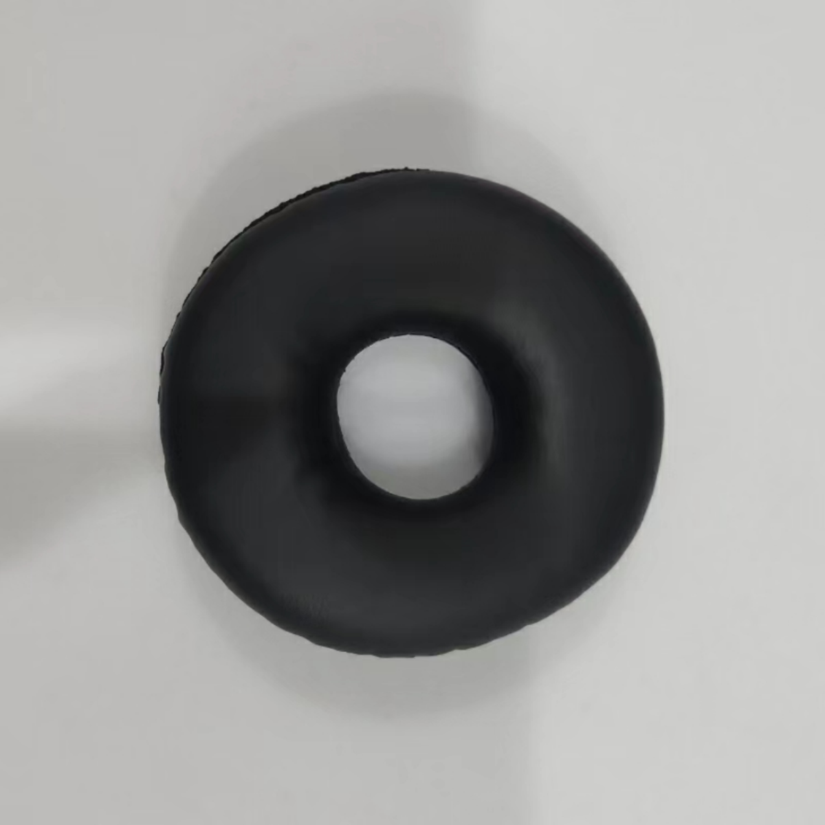 Schwarzes, donut-förmiges Objekt auf weißer Oberfläche. Scheint ein Kopfhörerkissen zu sein.