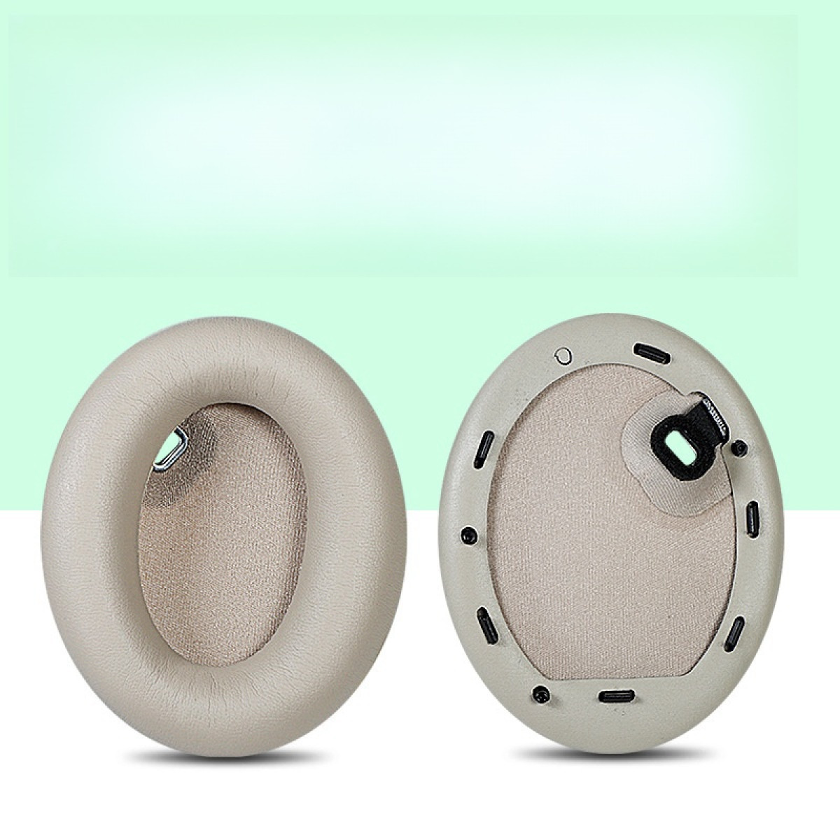 Dwie szare owalne wkładki do słuchawek. Beżowe wnętrze i czarne detale. Jasne tło.