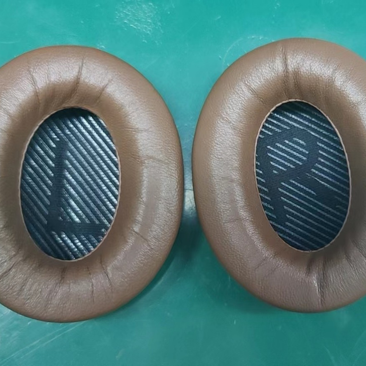 Dwie brązowe poduszki nauszniki do słuchawek. Wnętrze z materiałem i literami L i R.