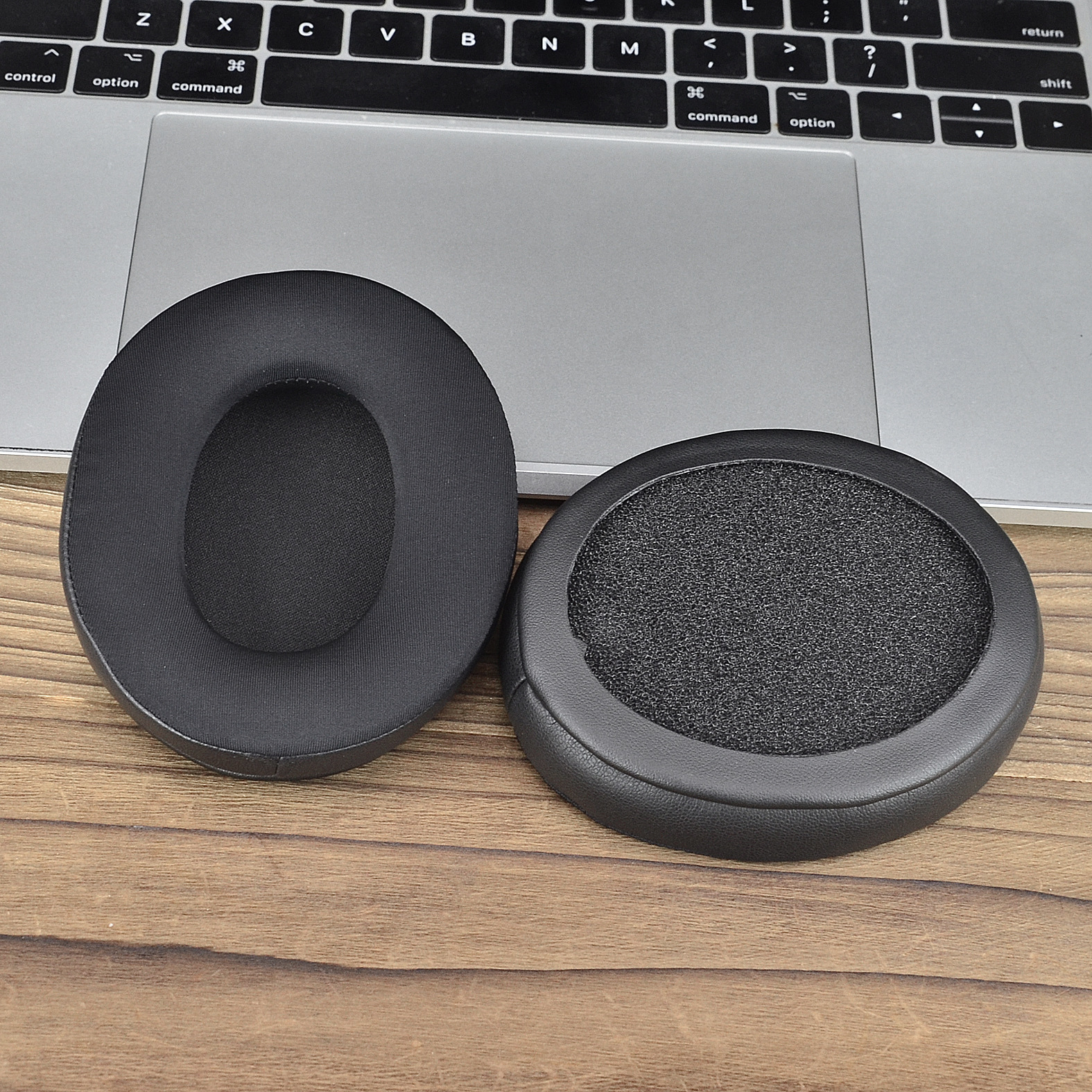 Due cuscinetti neri per cuffie sono su una superficie di legno vicino alla tastiera di un laptop.