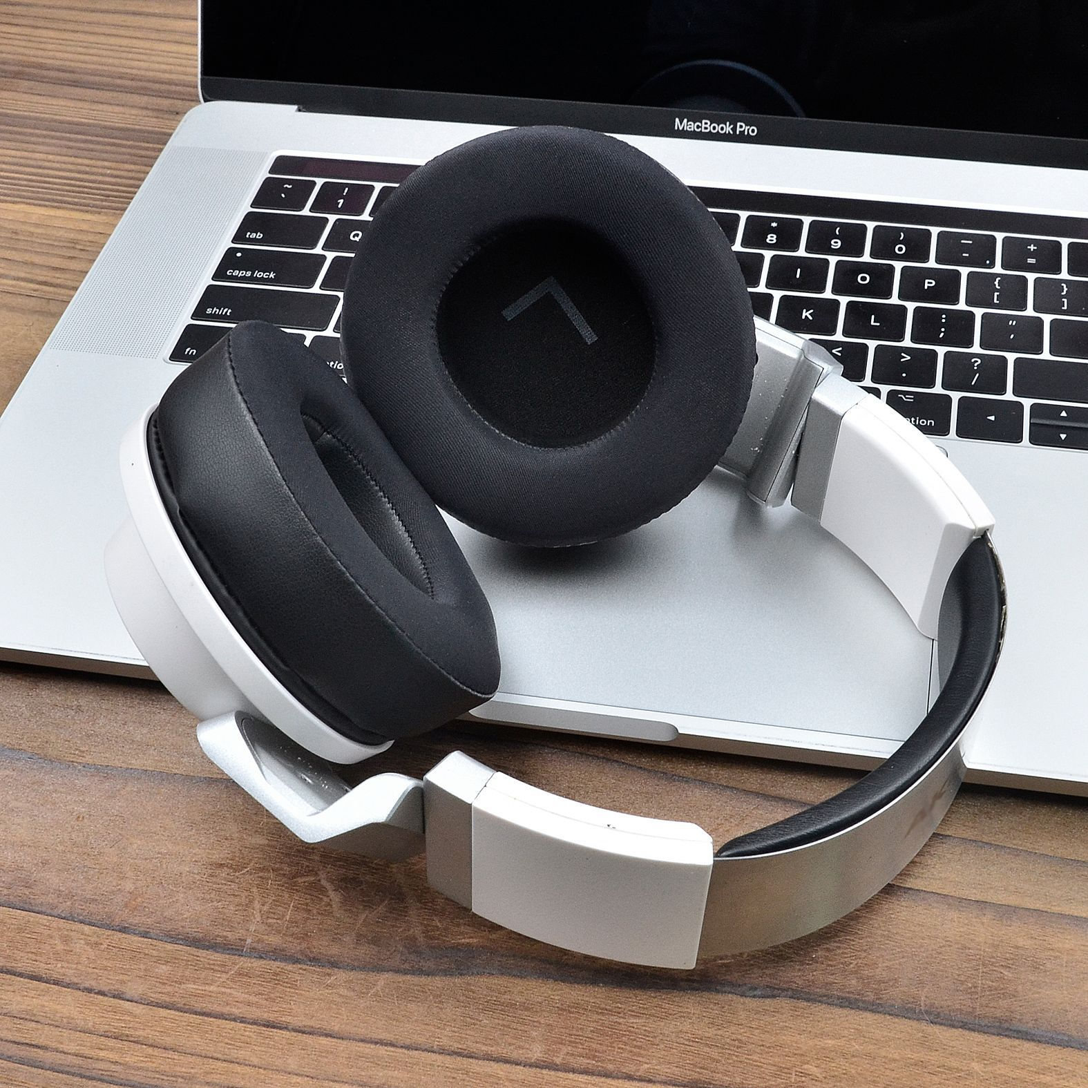 Biało-czarne słuchawki na laptopie. Tło: drewniany stół.