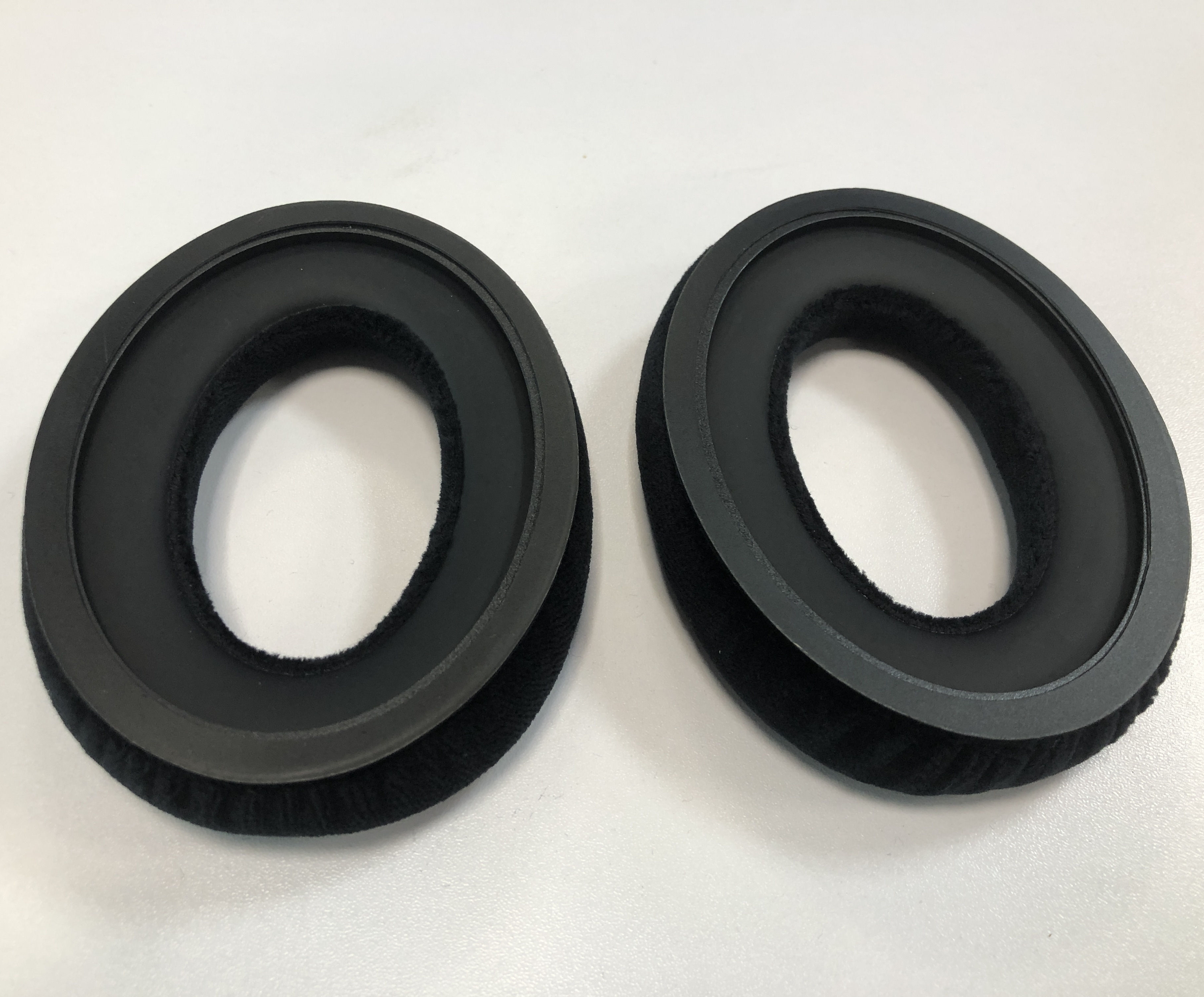 Dwie czarne owalne poduszki na uszy. Są okrągłe i mają okrągły pierścień.