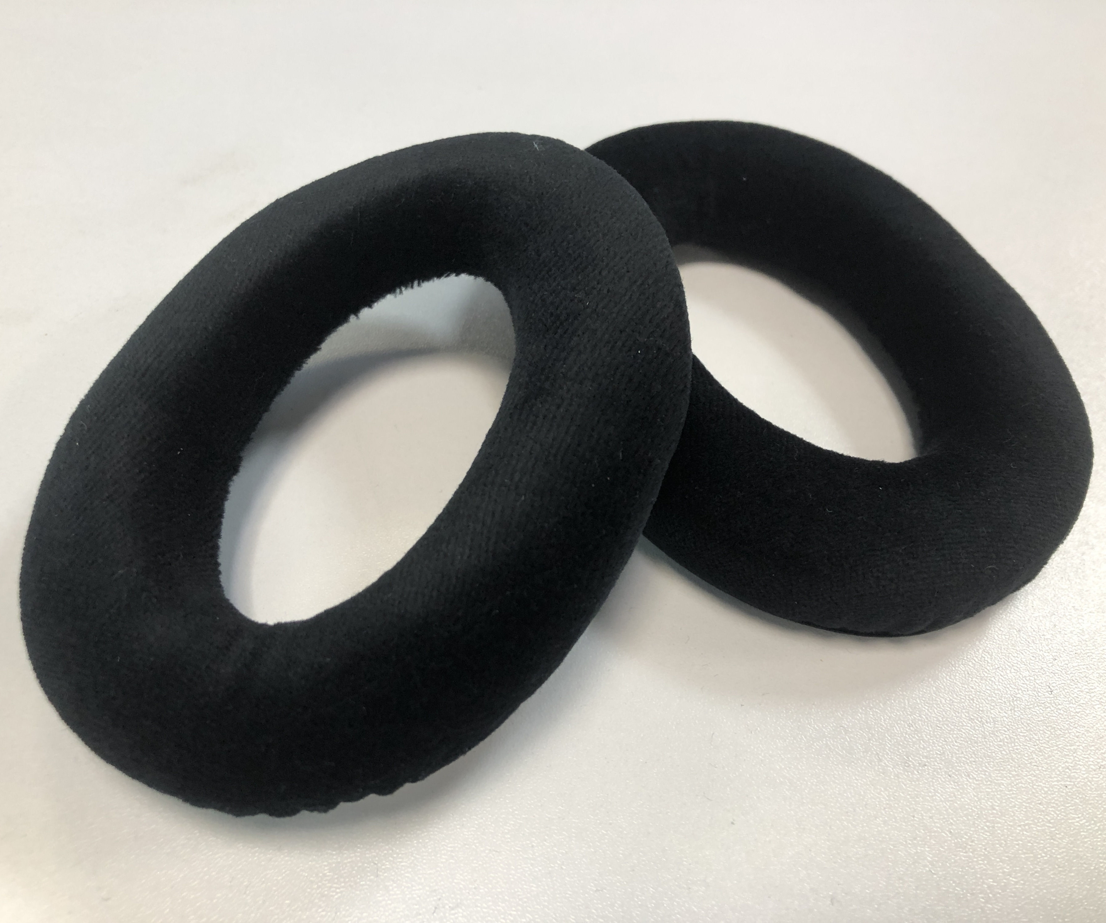Dwie czarne, owalne poduszki uszne z pianki, obok siebie, na białej powierzchni.