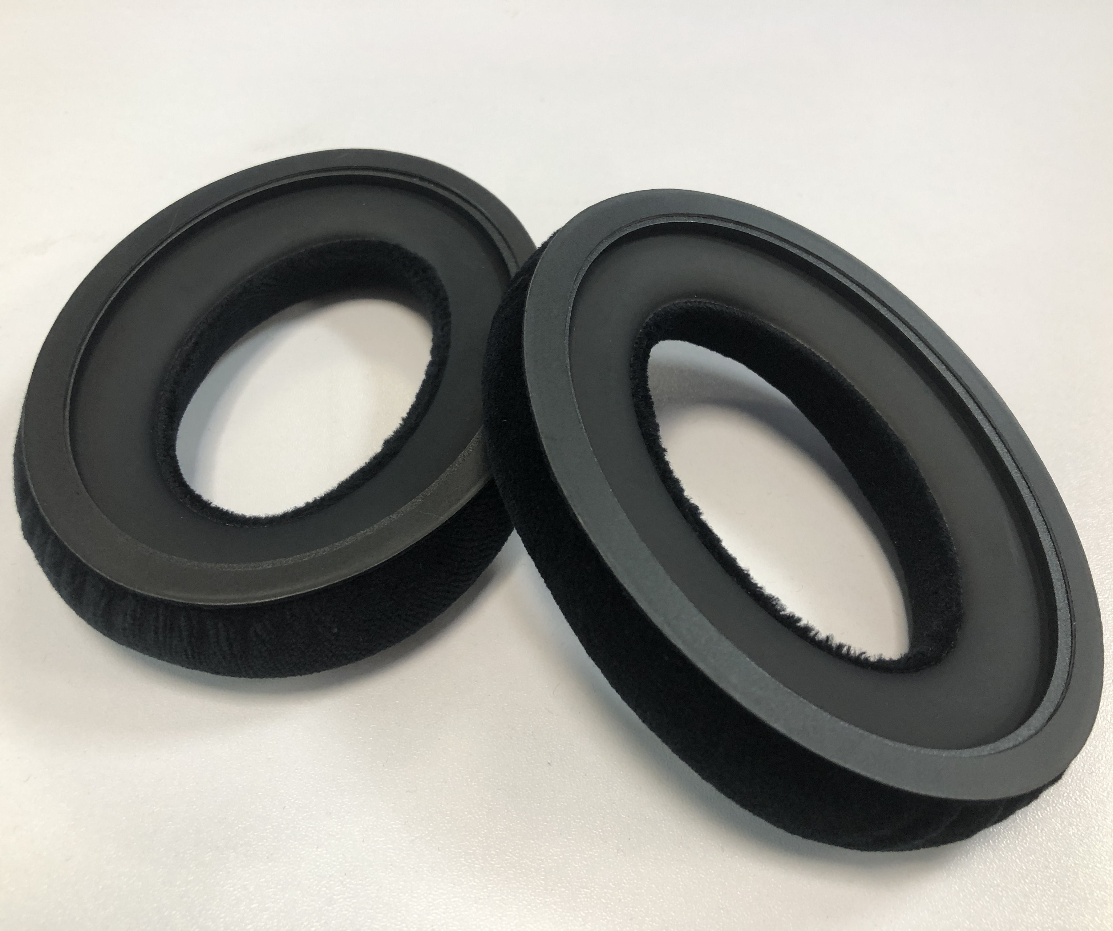 Dwie czarne nauszniki. Są okrągłe i mają miękką, czarną powierzchnię z tkaniny.