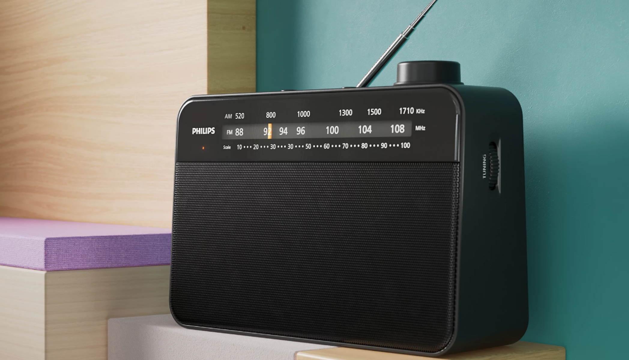Czarny radioodbiornik Philips z pokrętłem strojenia i anteną. Stoi na drewnianej półce na tle turkusowego tła.