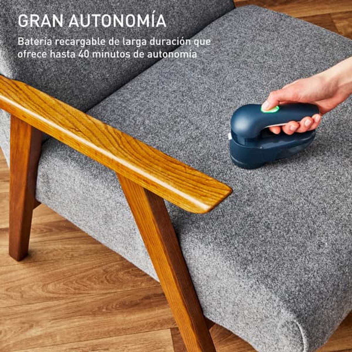 Una mano usa un leva pelucchi su un divano grigio, pavimento in legno in vista.