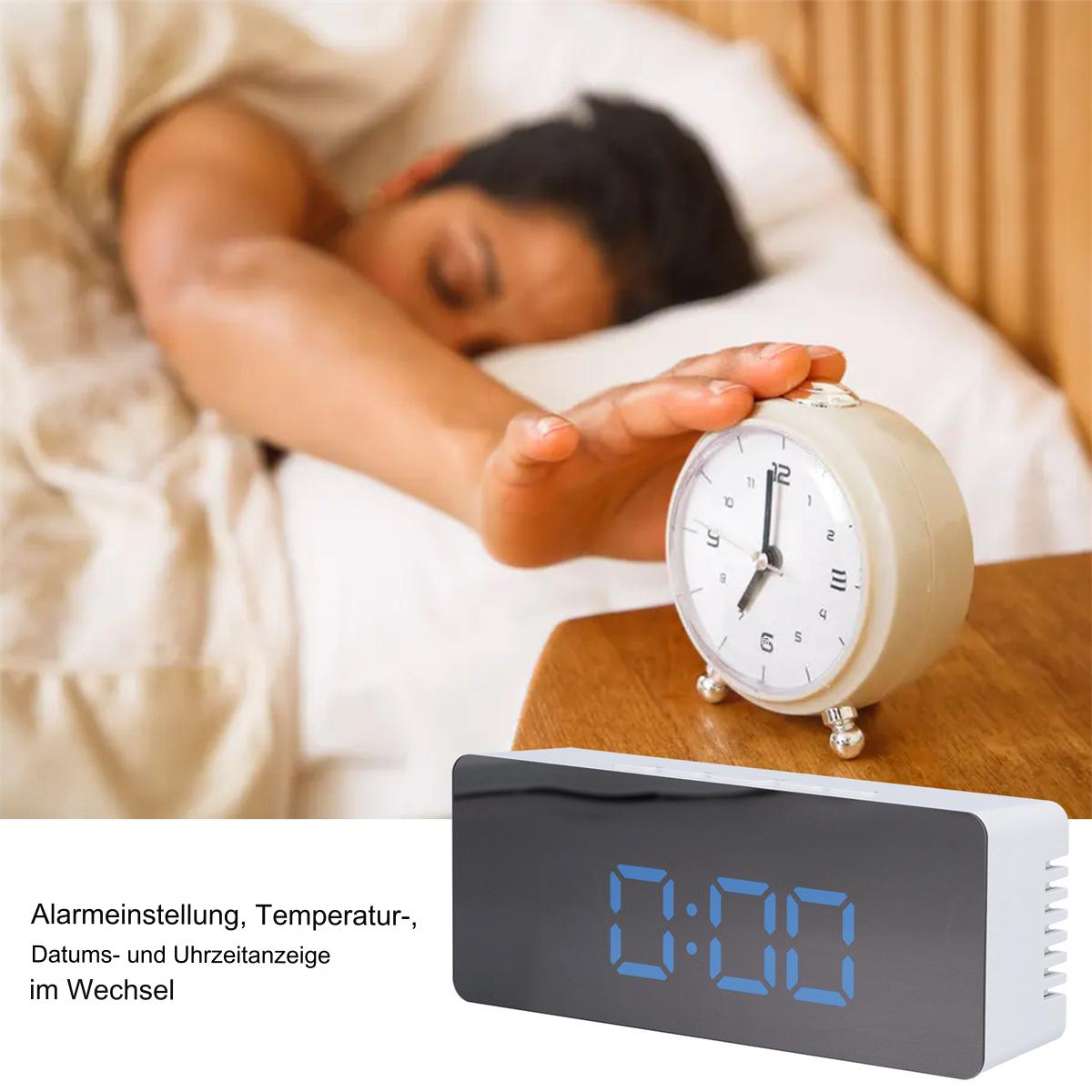 Eine Person greift nach einem Wecker auf einem Nachttisch. Eine Digitaluhr ist ebenfalls vorhanden.