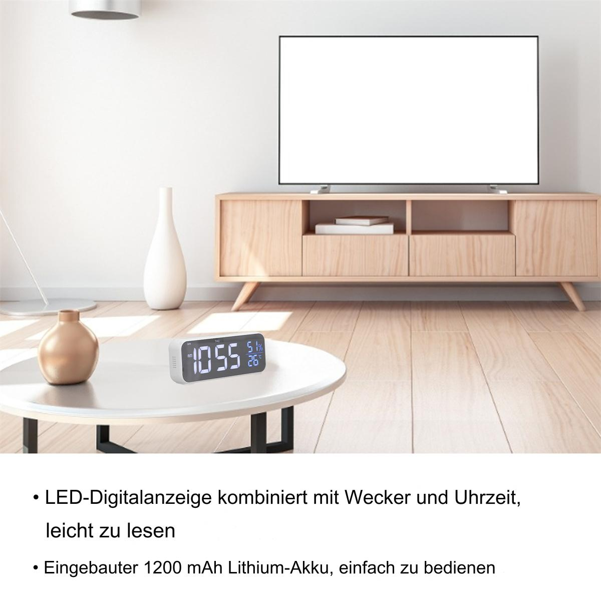 Digitaluhr auf Tisch mit TV im Hintergrund, zeigt Zeit und Temperatur an.