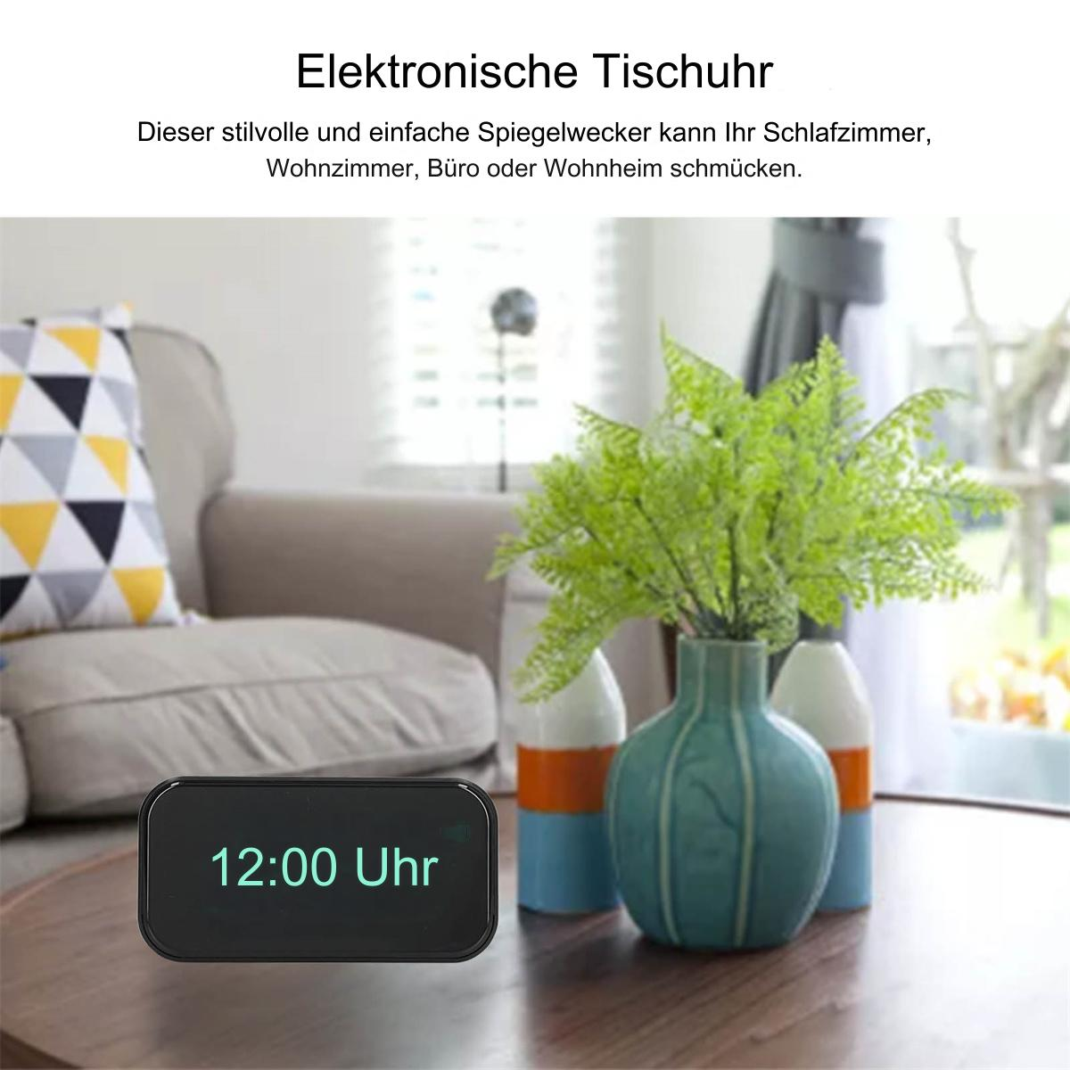 Digitaluhr, die 12:00 Uhr auf einem Tisch anzeigt, mit einer Vase mit Pflanzen im Hintergrund.