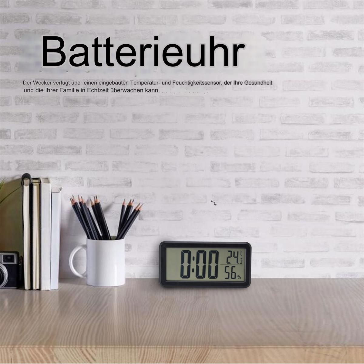 Digitaluhr zeigt 0:00, 24 Grad und 56%. Bleistifte in einem Becher und Bücher sind links.