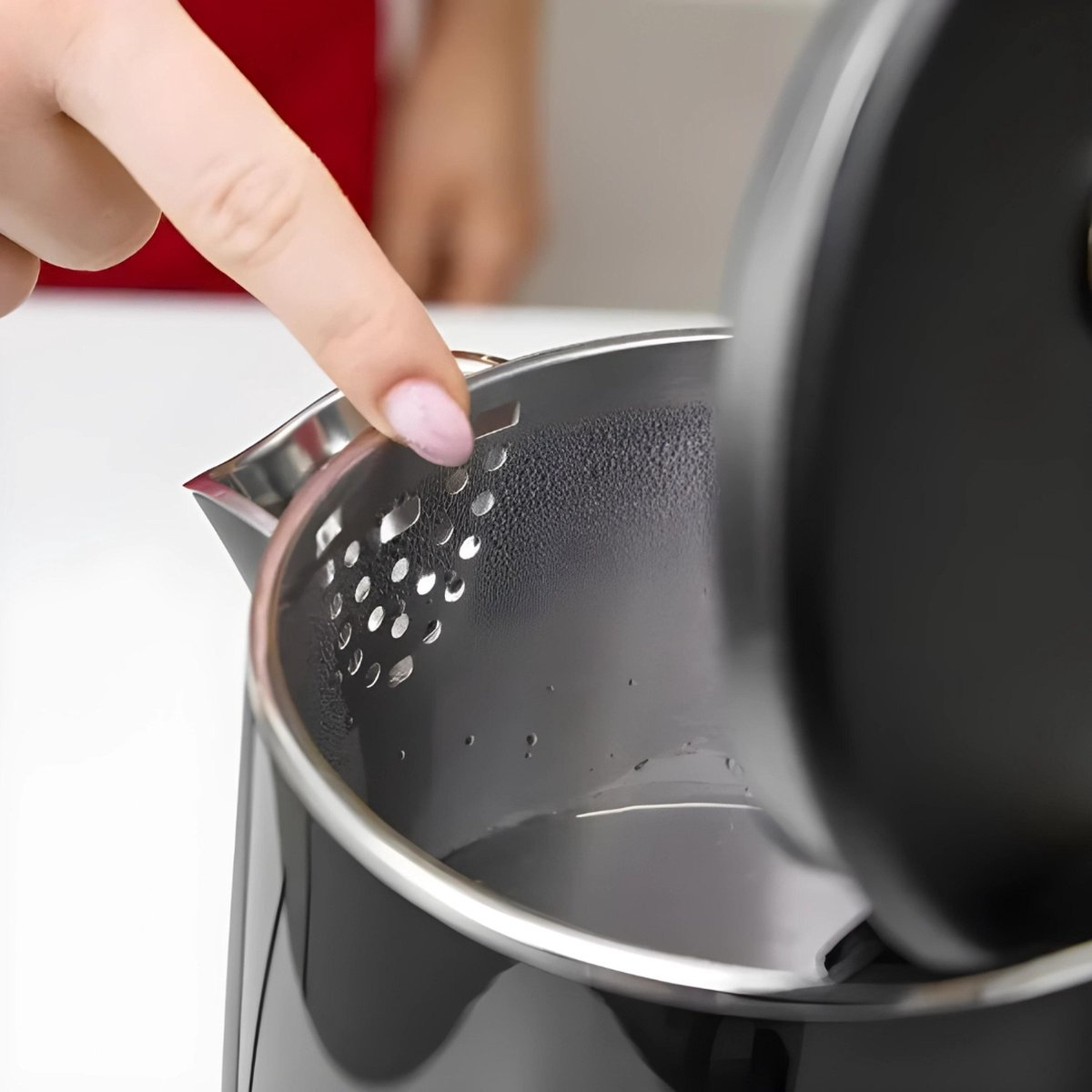 Eine Hand berührt die Innenseite eines schwarzen Wasserkochers mit sichtbaren Wassertropfen.
