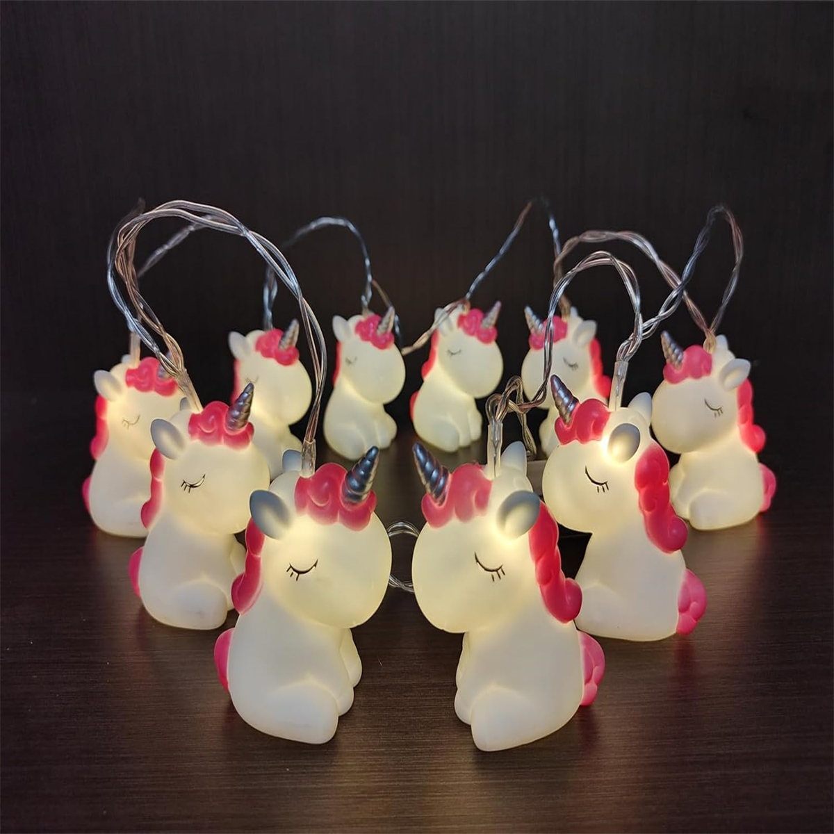 Lichterketten mit Einhorn-förmigen Lichtern, rosa Mähnen und Hörnern. Sie befinden sich auf dunklem Hintergrund, beleuchtet.