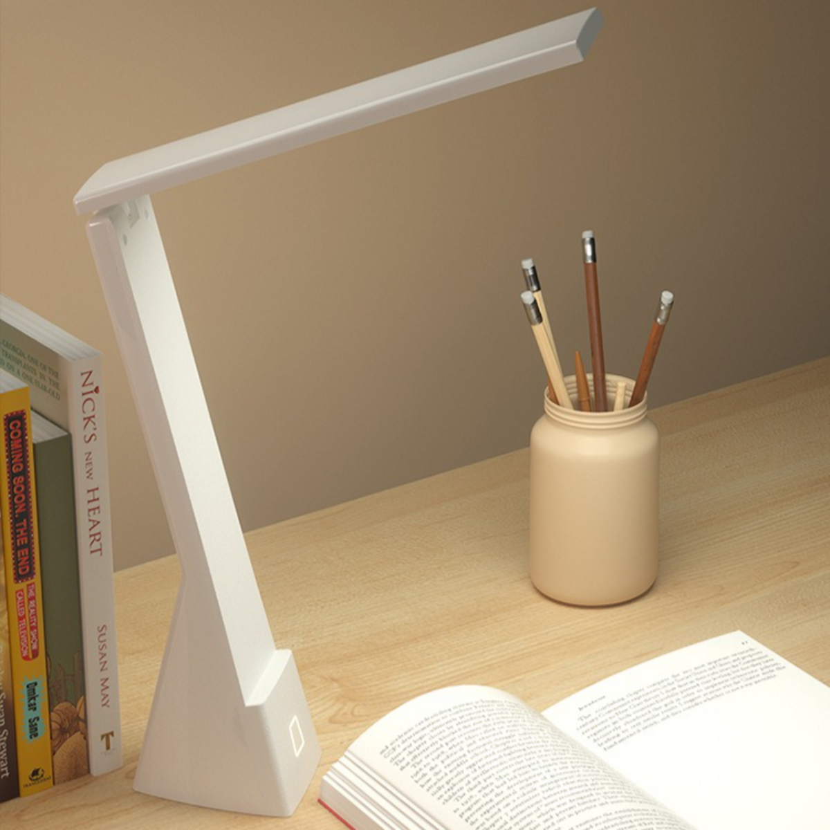 Eine weiße Schreibtischlampe mit einem Buch, Bleistiften und einem weiteren Buch auf einem Holzschreibtisch.