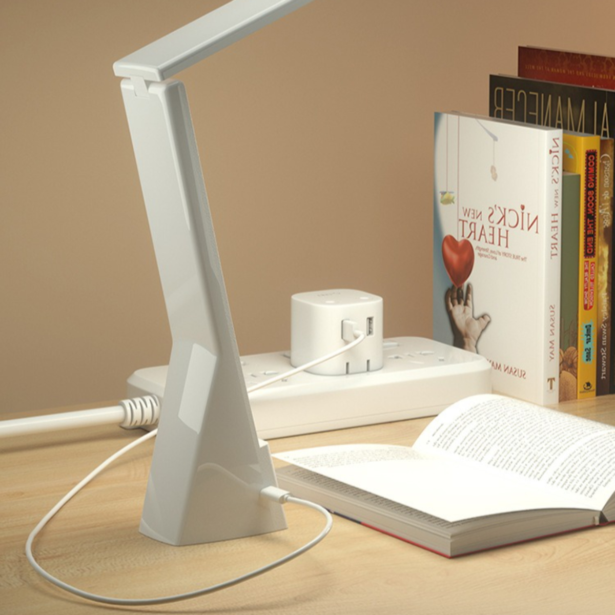 Weiße Schreibtischlampe mit Ladeanschluss, Büchern und einem offenen Buch auf einem Holzschreibtisch.