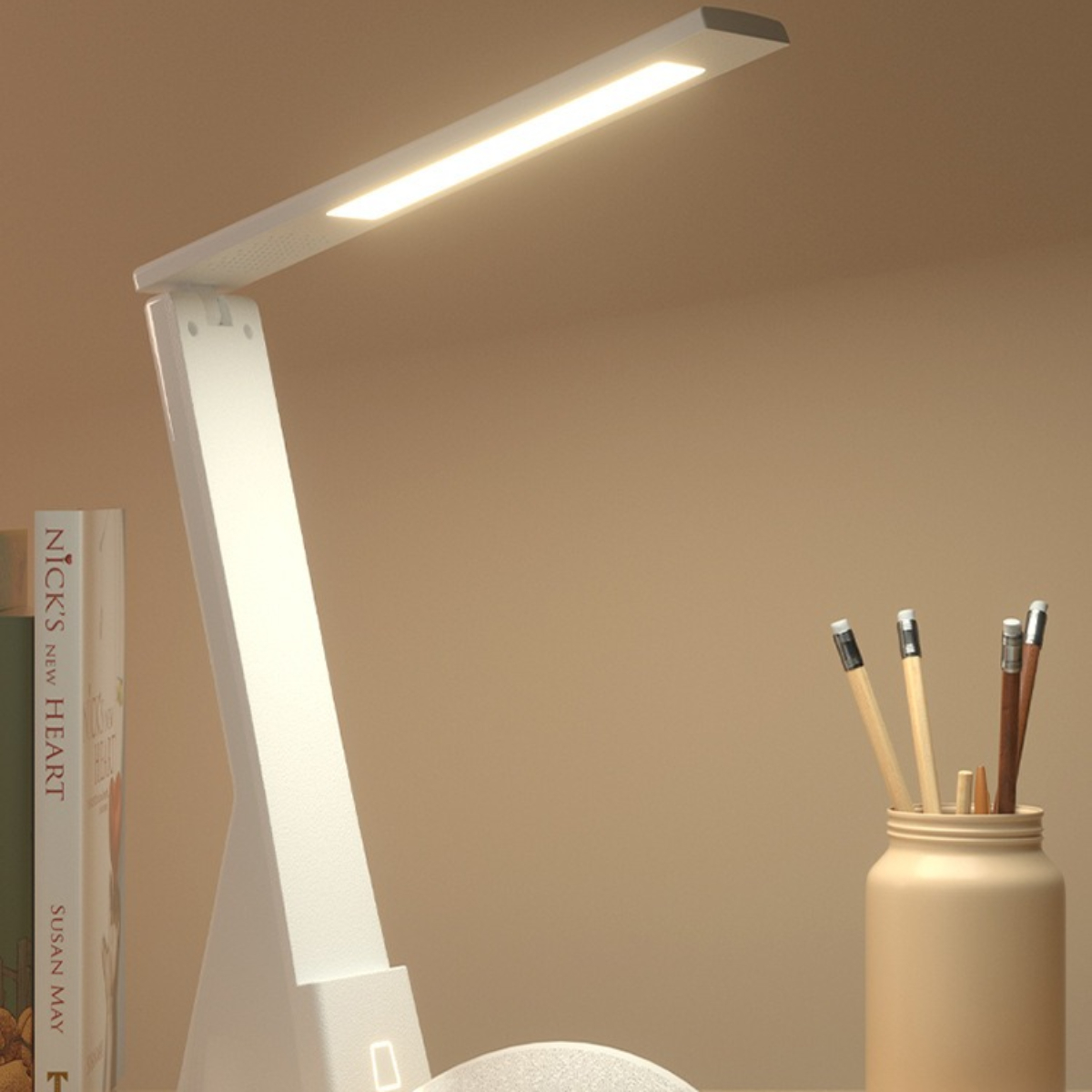 Weiße Schreibtischlampe mit langem Licht. Bücher und Bleistifte in einem Glas befinden sich auf dem Schreibtisch. Beigefarbener Hintergrund.
