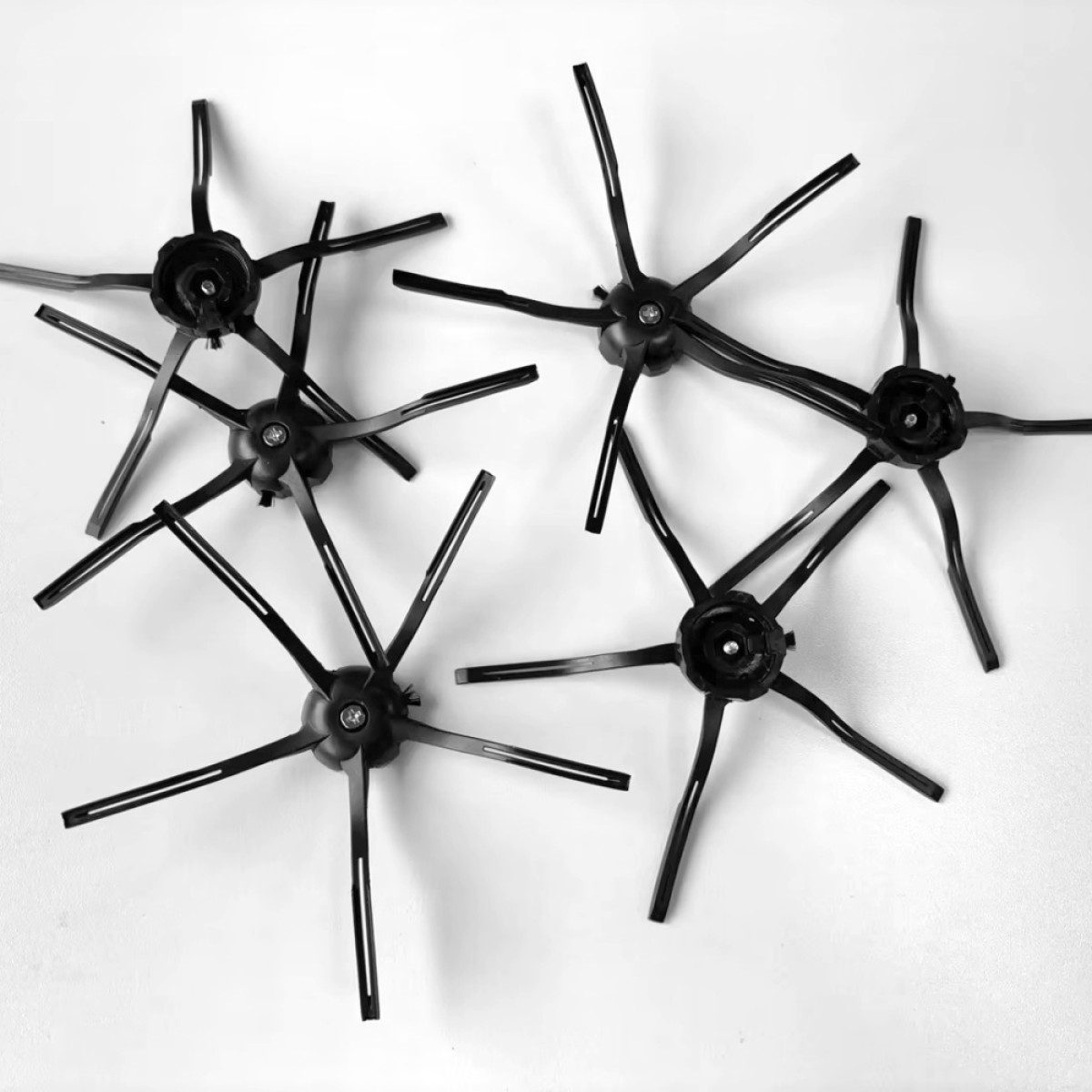 Czarne szczotki do odkurzacza na białej powierzchni. Posiadają liczne ramiona z centralnego punktu.