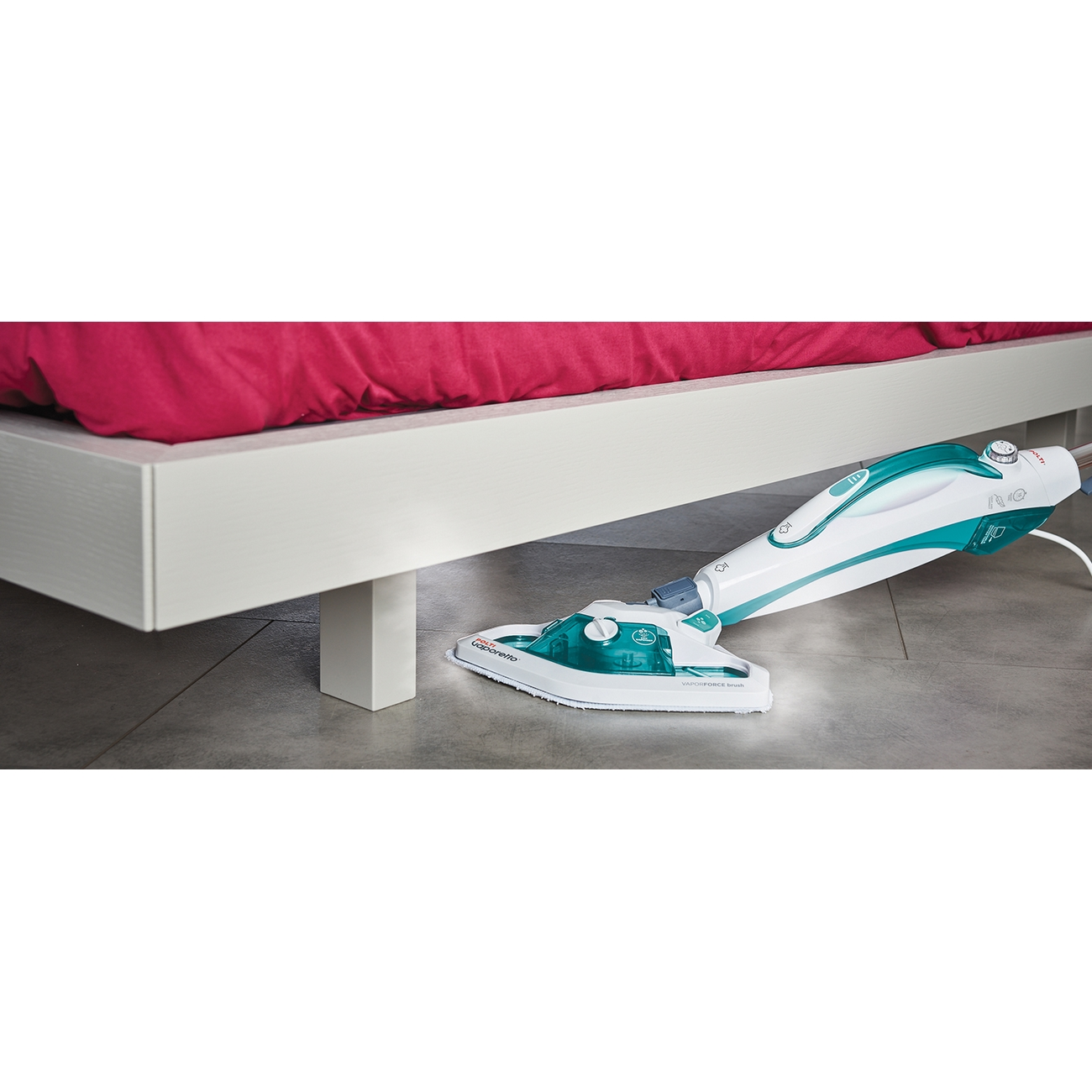 Biało-zielony odkurzacz parowy czyszczący pod białym łóżkiem. Podłoga jest szara.