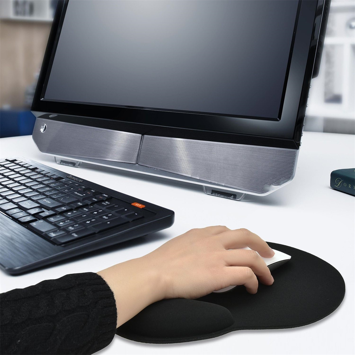 Eine Person, die eine Computermaus auf einem Mauspad in der Nähe einer Tastatur und eines Bildschirms verwendet.