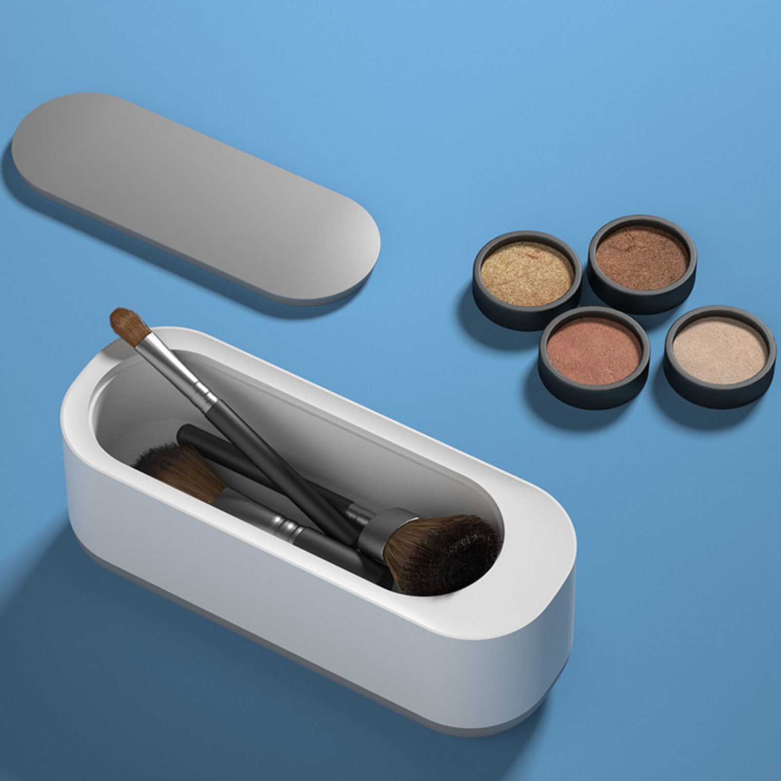 Ein weißer Ultraschallreiniger mit Make-up-Pinseln im Inneren und Lidschatten auf blauer Oberfläche.