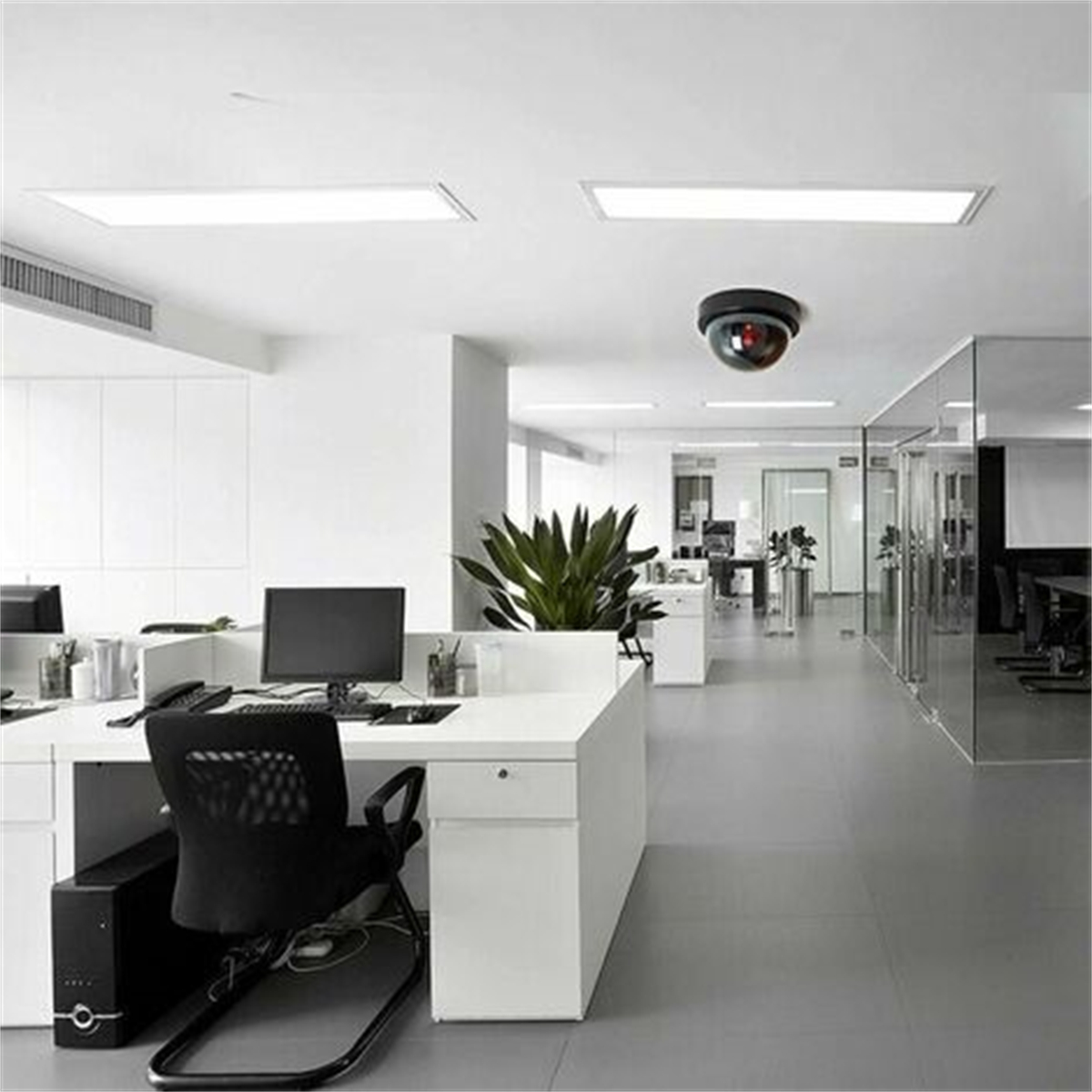 Modernes Büro mit weißen Schreibtischen, schwarzen Stühlen und Überwachungskamera.