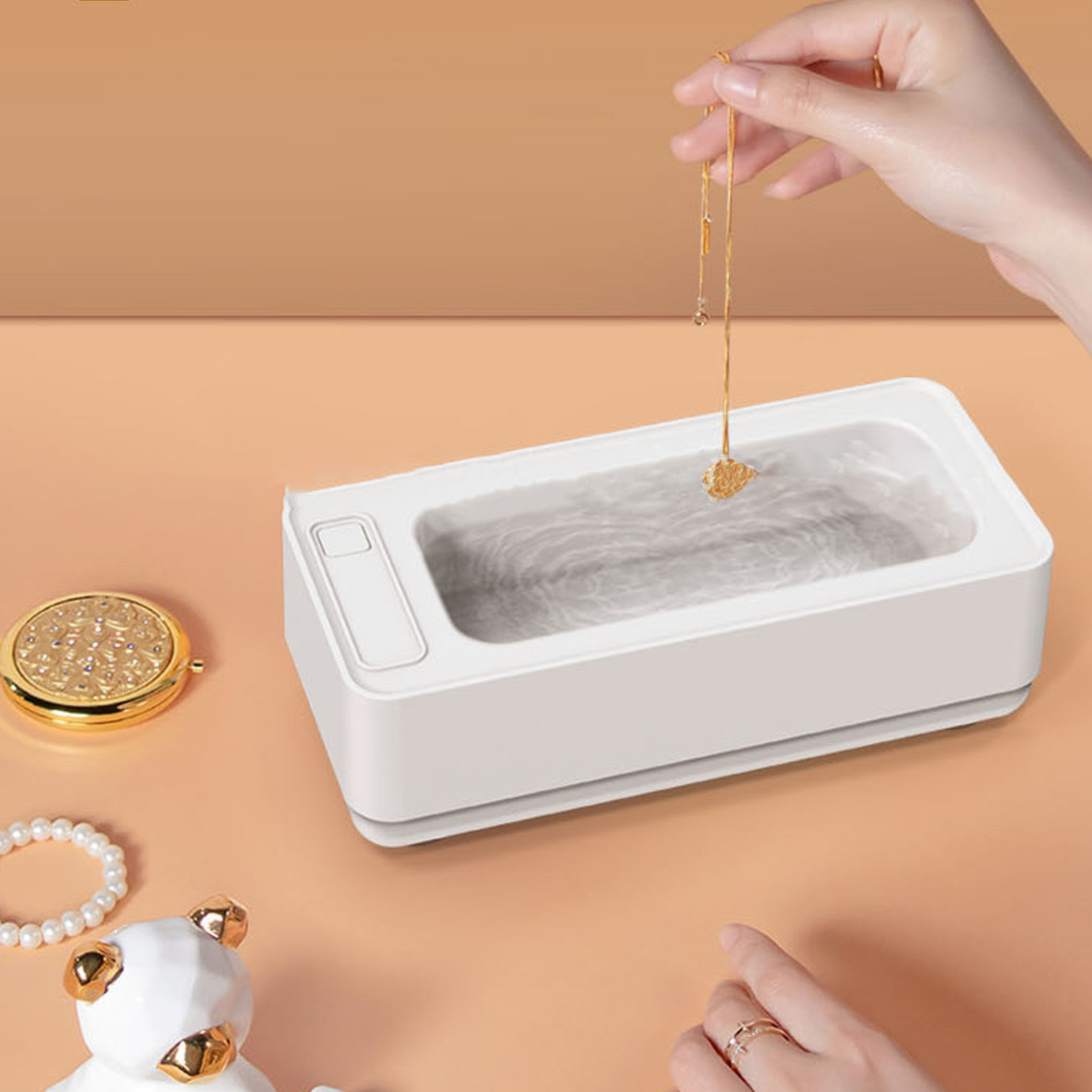 Eine Hand legt eine Halskette in eine weiße Schmuckreinigungsmaschine.