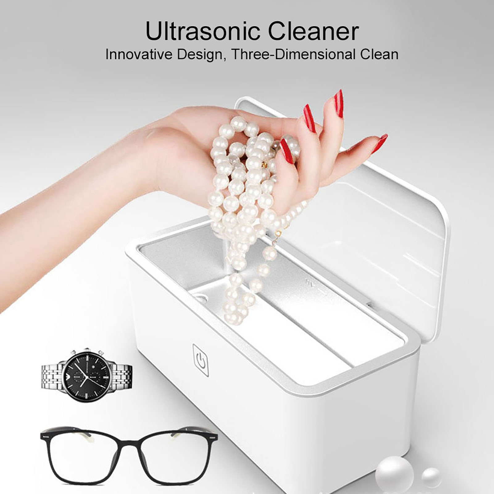Eine Hand hält eine Perlenkette über einem Ultraschallreiniger mit einer Uhr und einer Brille daneben.