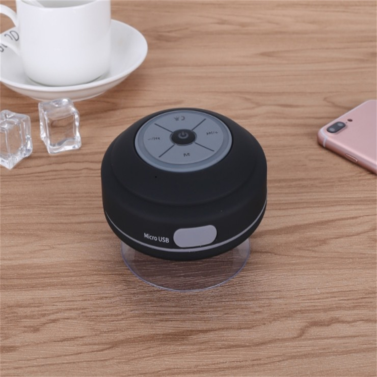 Schwarzer wasserdichter Lautsprecher mit Knöpfen und Micro-USB-Anschluss auf Holztisch.