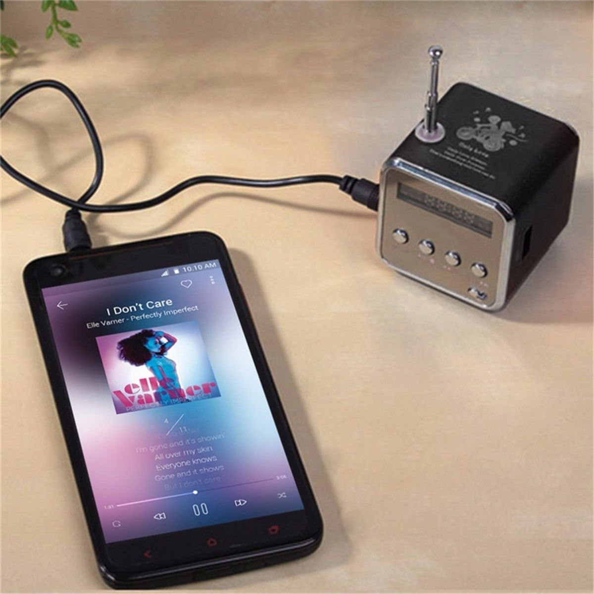 Ein Smartphone zeigt eine Musik-App mit einem spielenden Song. Ein kleines Retro-Radio ist per Kabel verbunden.