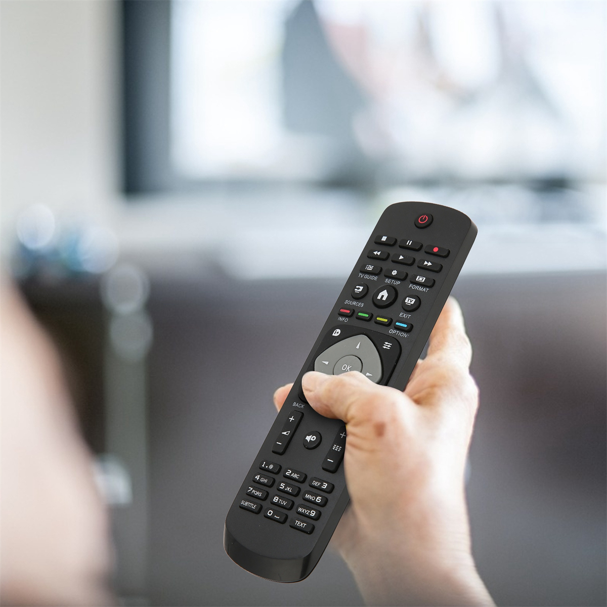 Eine schwarze TV-Fernbedienung wird in der Hand gehalten. Der Hintergrund ist unscharf.