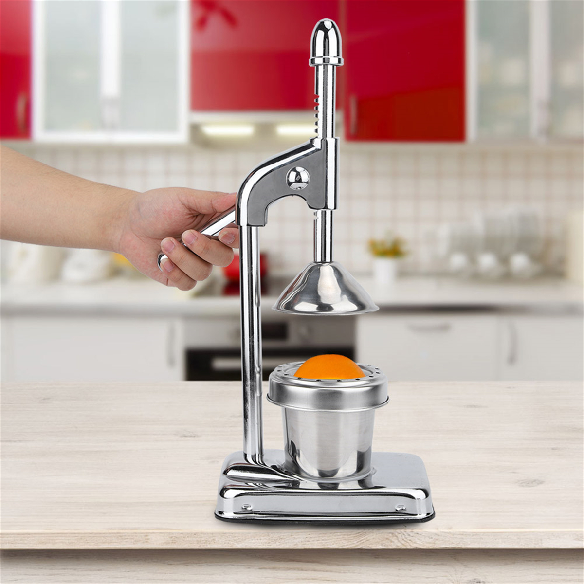 Eine Person, die eine Orange mit einer manuellen Saftpresse aus Edelstahl auf einem Holztisch auspresst.
