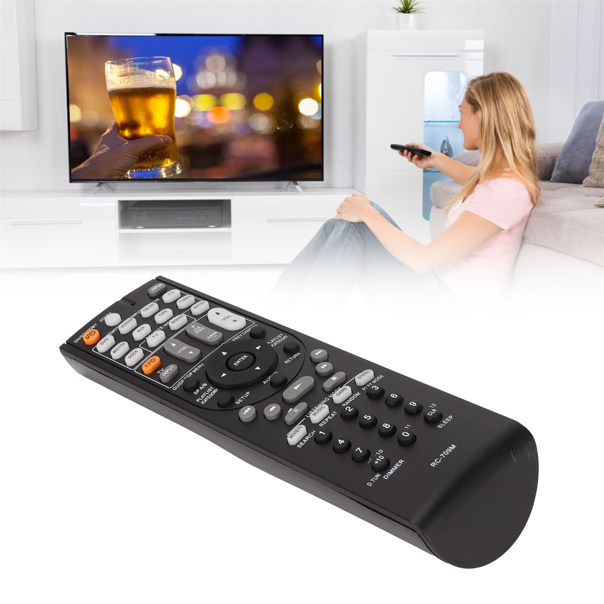 Schwarze Fernbedienung mit vielen Tasten, Frau hält sie, Fernseher im Hintergrund.