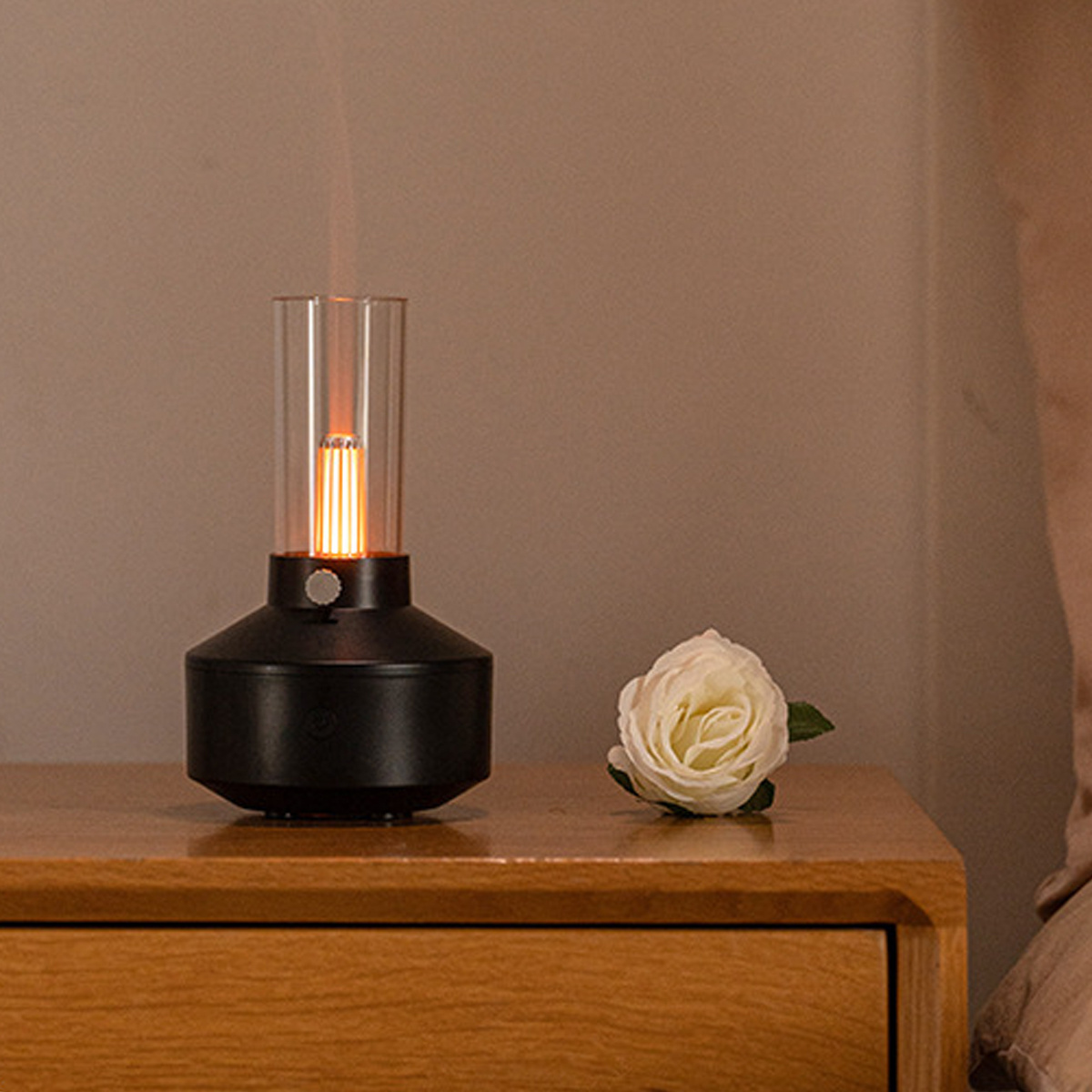 Eine schwarze Nachttischlampe mit einem Glasrohr mit Leuchteffekt, neben einer weißen Rose auf einer Holzoberfläche.