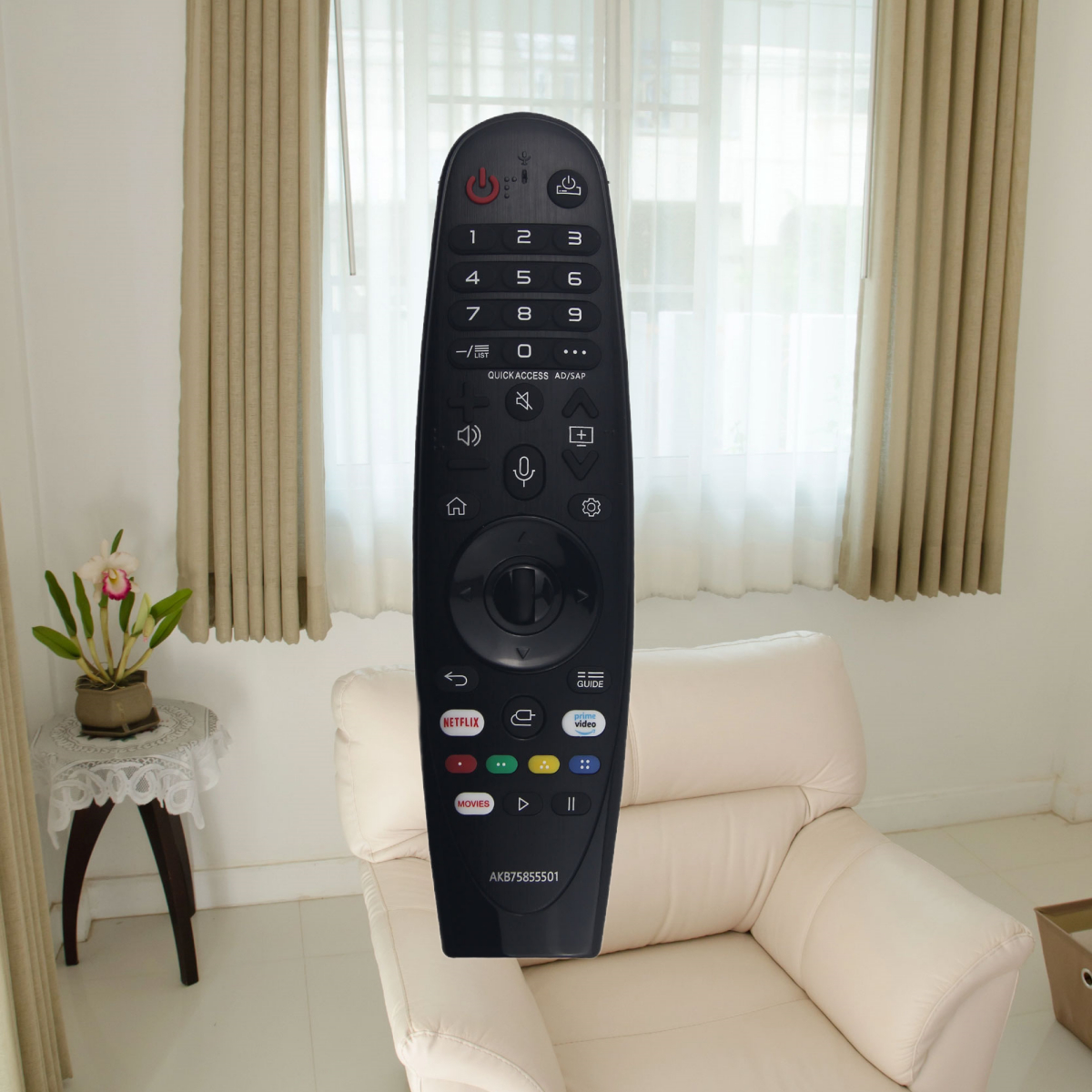 Schwarze TV-Fernbedienung auf einem beigen Sofa, in einem Raum mit Vorhängen und einer Blume.
