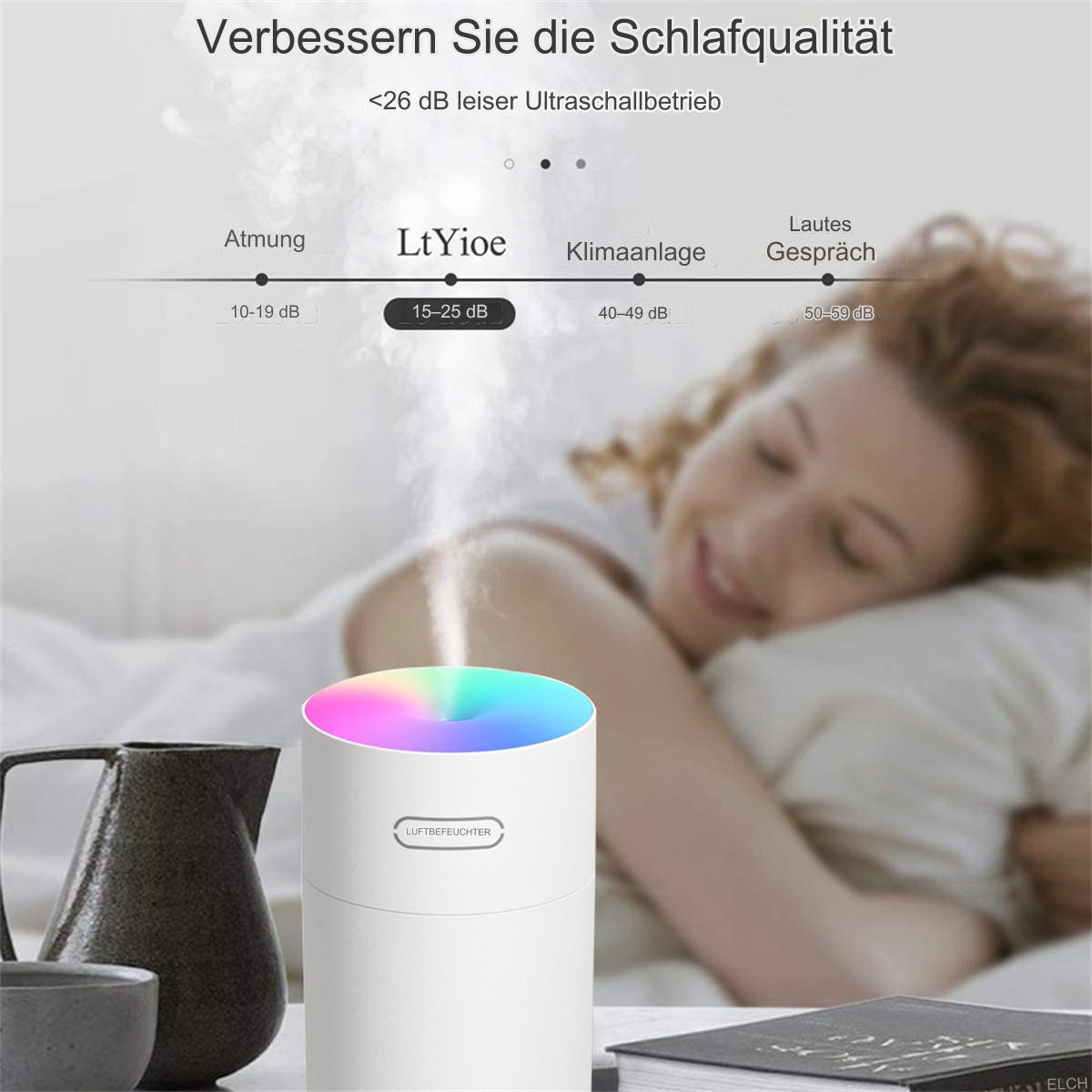 Ein weißer Luftbefeuchter mit farbwechselndem Deckel, neben einer Karaffe und einer schlafenden Person.