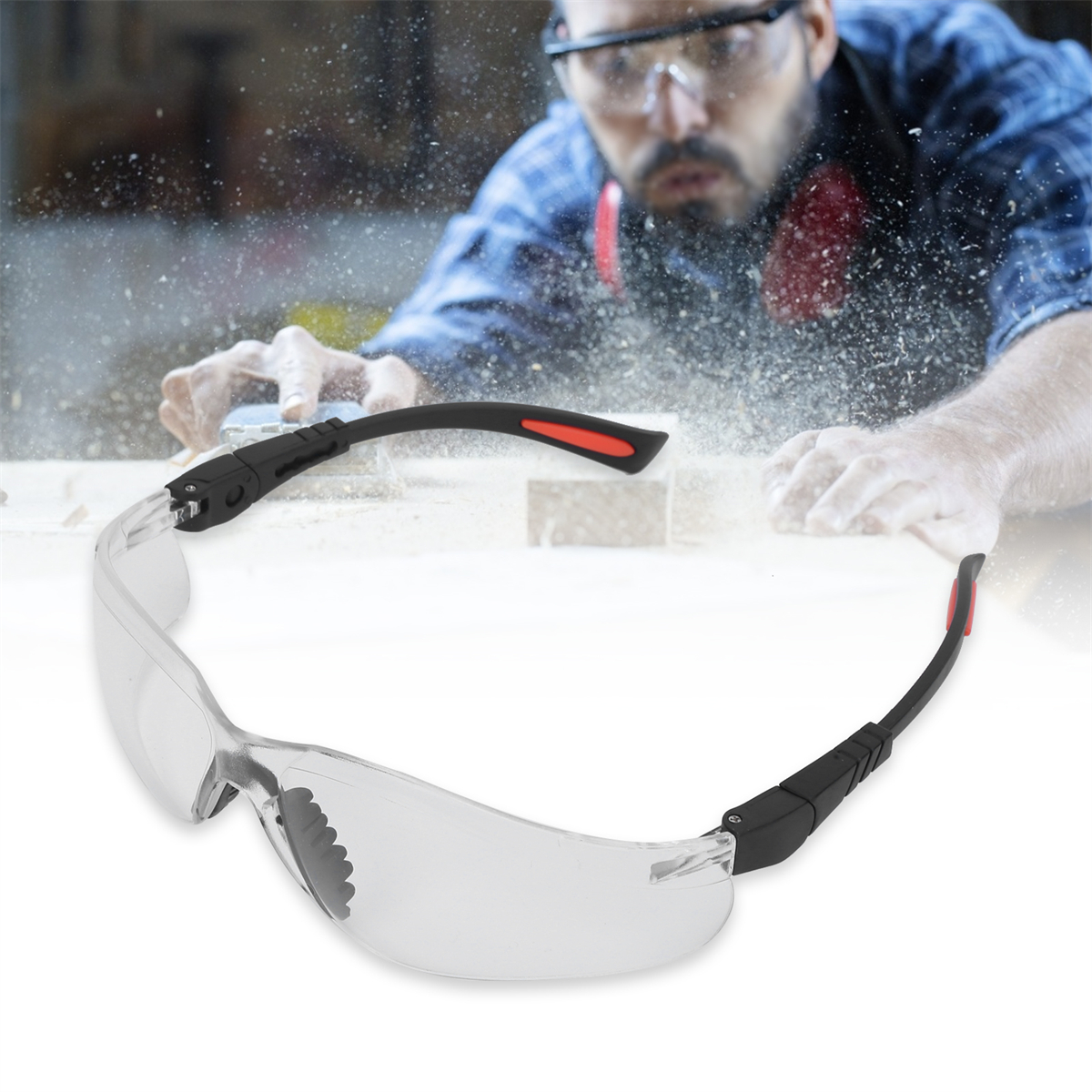Schutzbrille mit klaren Gläsern, schwarzen Bügeln mit roten Akzenten, vor einem Holzarbeiter.